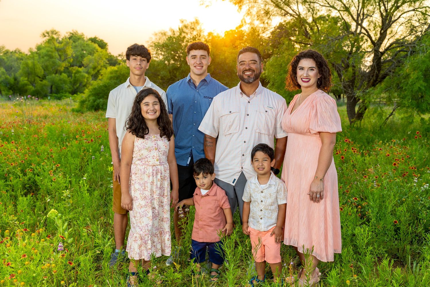 Happy family of seven posing in a wildflower meadow during golden hour sunset.