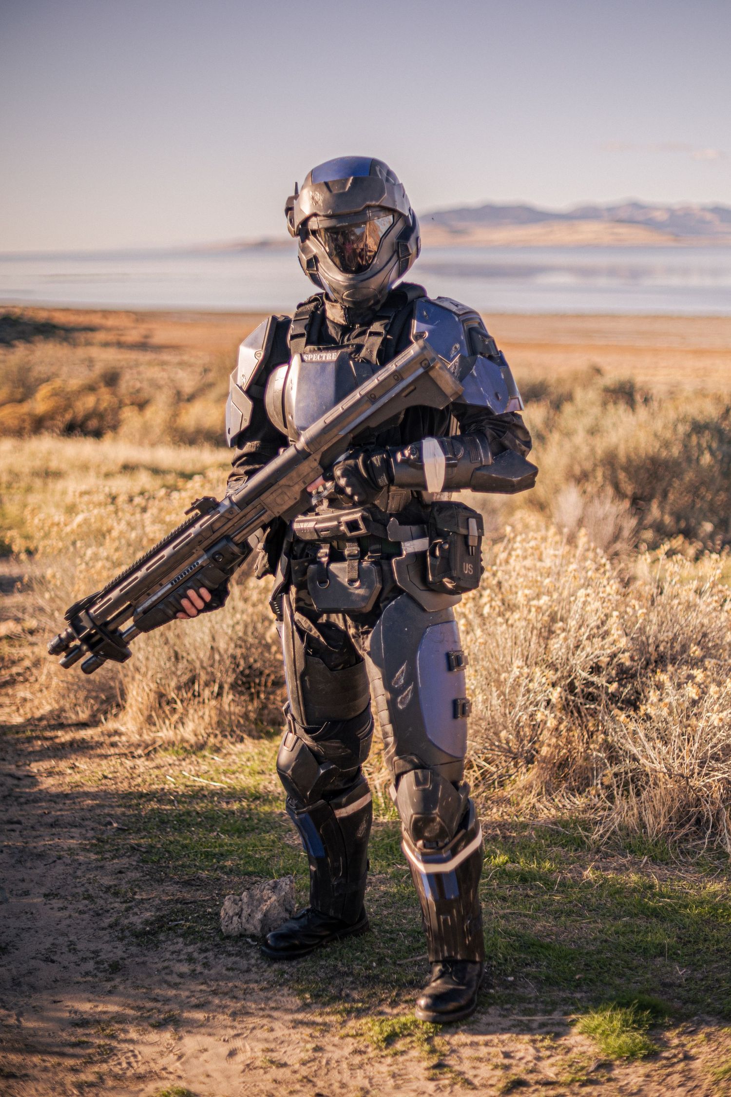 Person in futuristic sci-fi military armor suit holding large weapon outdoors in arid landscape.