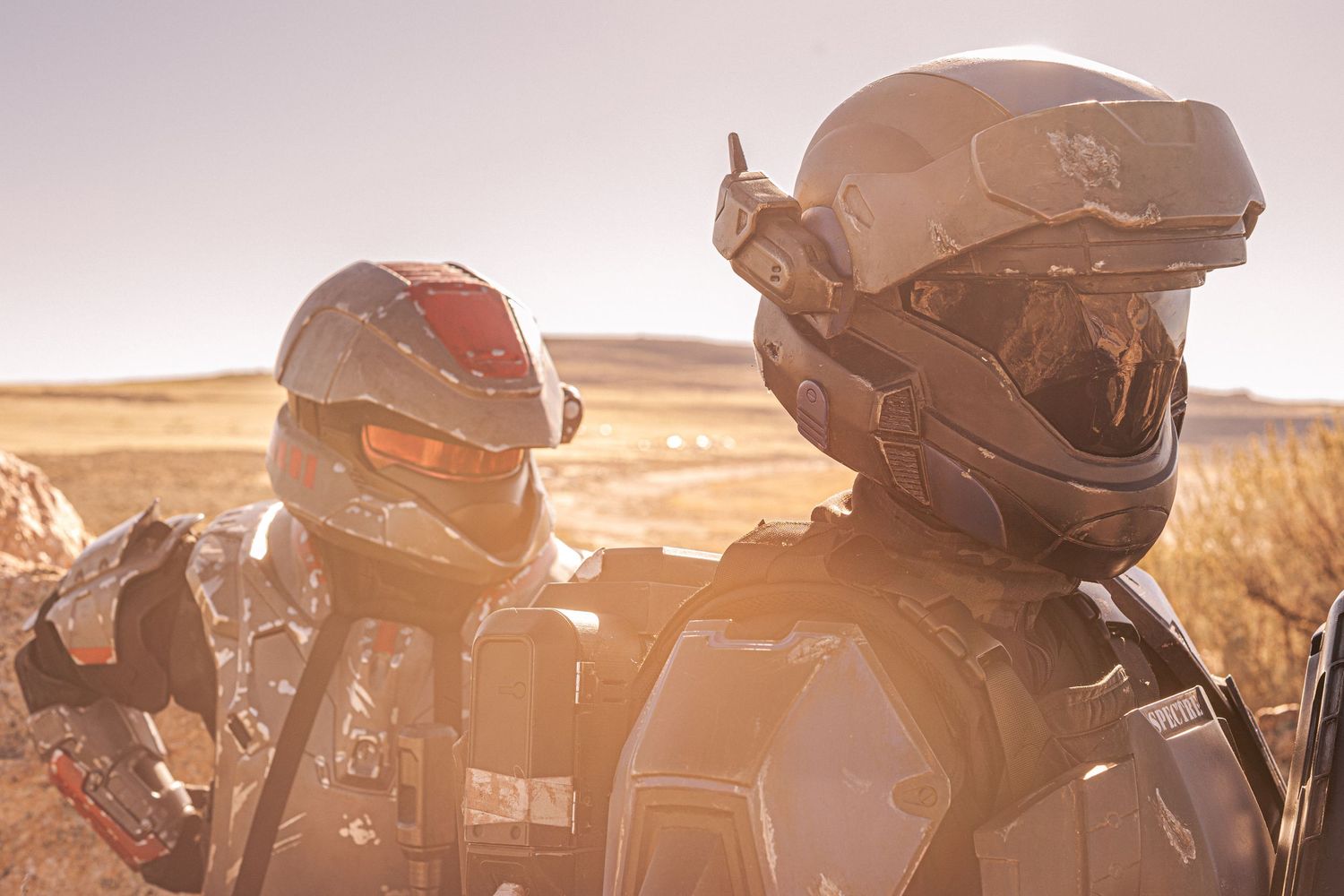 Two people wearing futuristic Halo-style helmets and armor in a sunlit desert landscape.