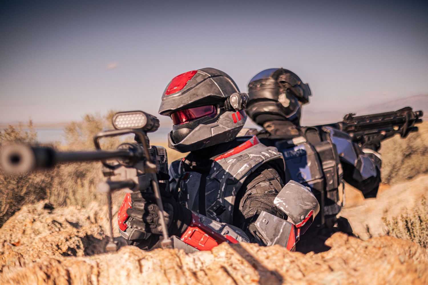 Close-up of airsoft players in sci-fi tactical armor aiming rifles in desert terrain.