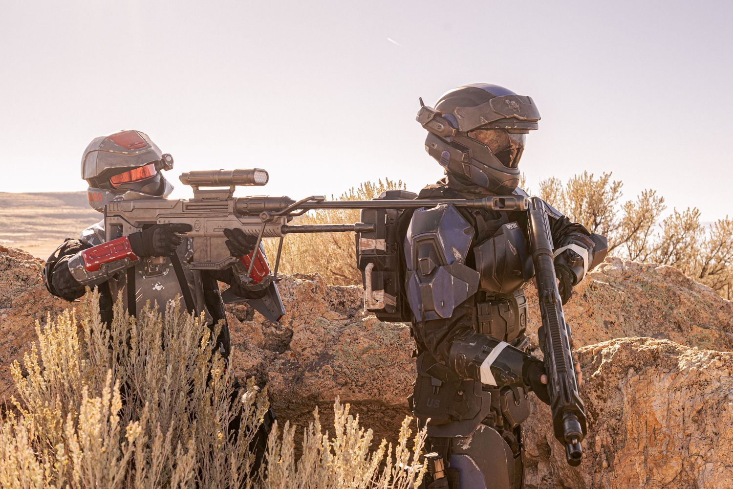 Two sci-fi armored cosplayers with rifles patrolling desert scrubland terrain.
