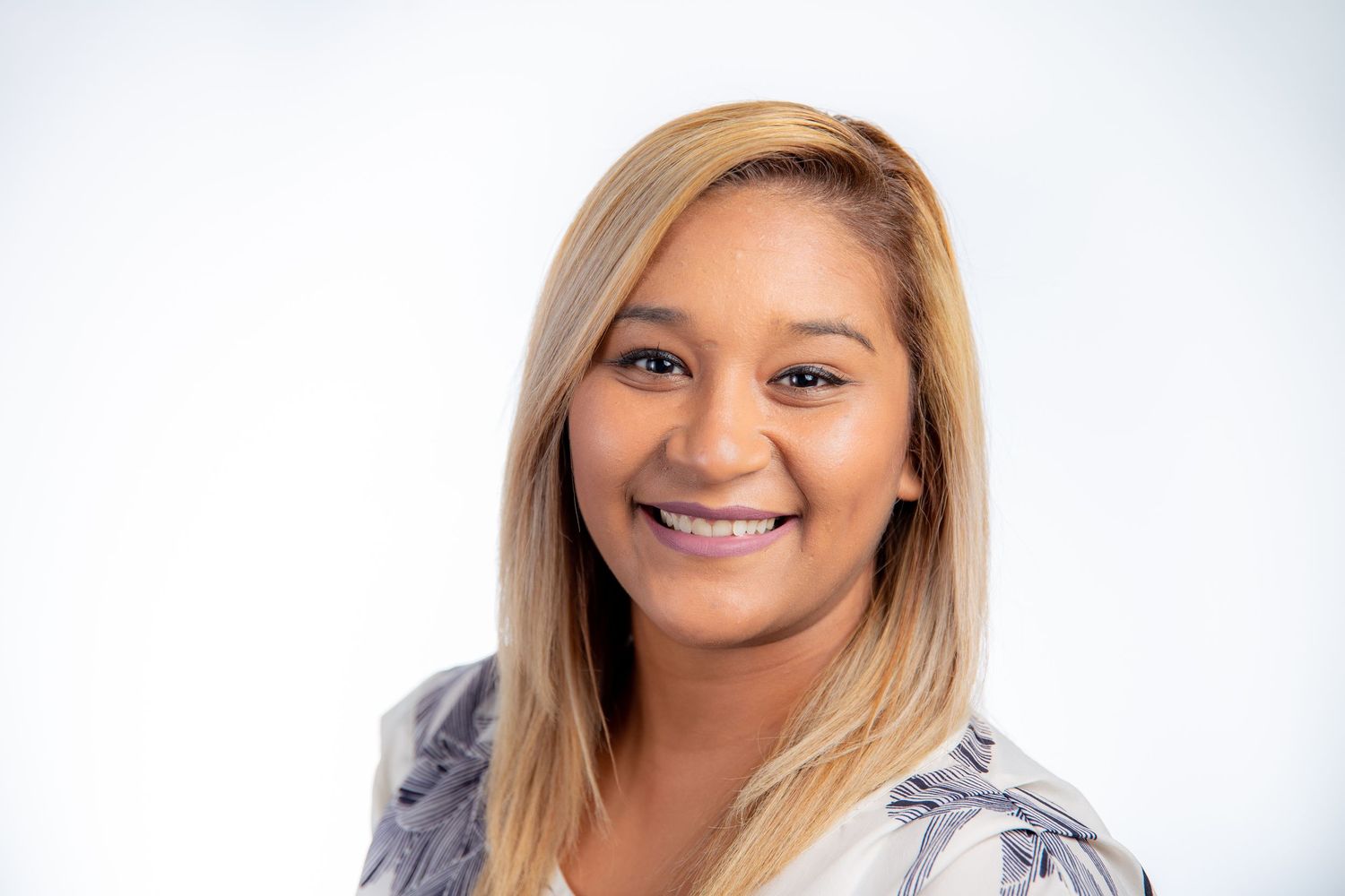 Professional headshot of smiling woman with blonde hair wearing floral blouse on white background.