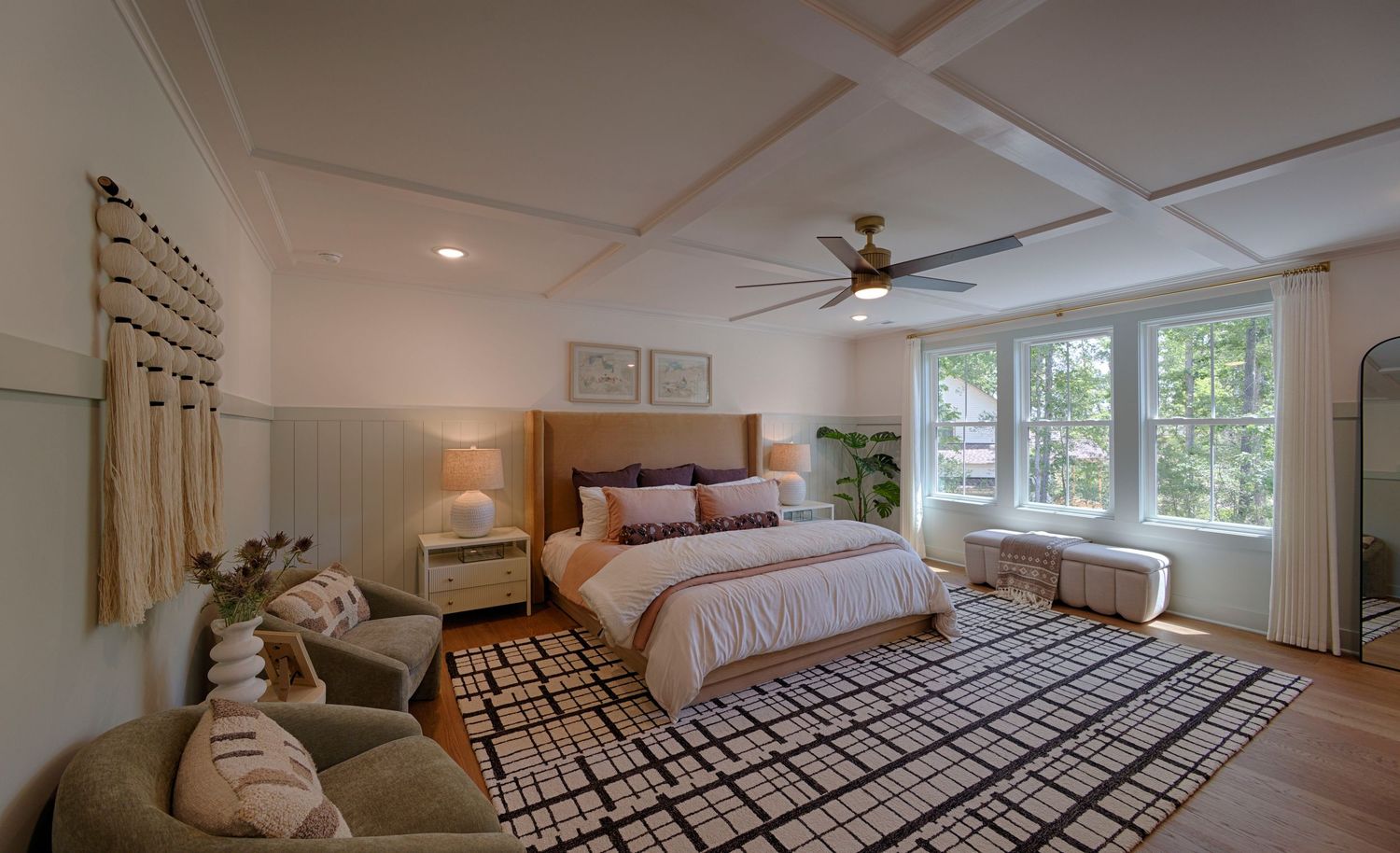 Spacious master bedroom with coffered ceiling, ceiling fan, geometric rug, upholstered bed, and bohemian wall decor.