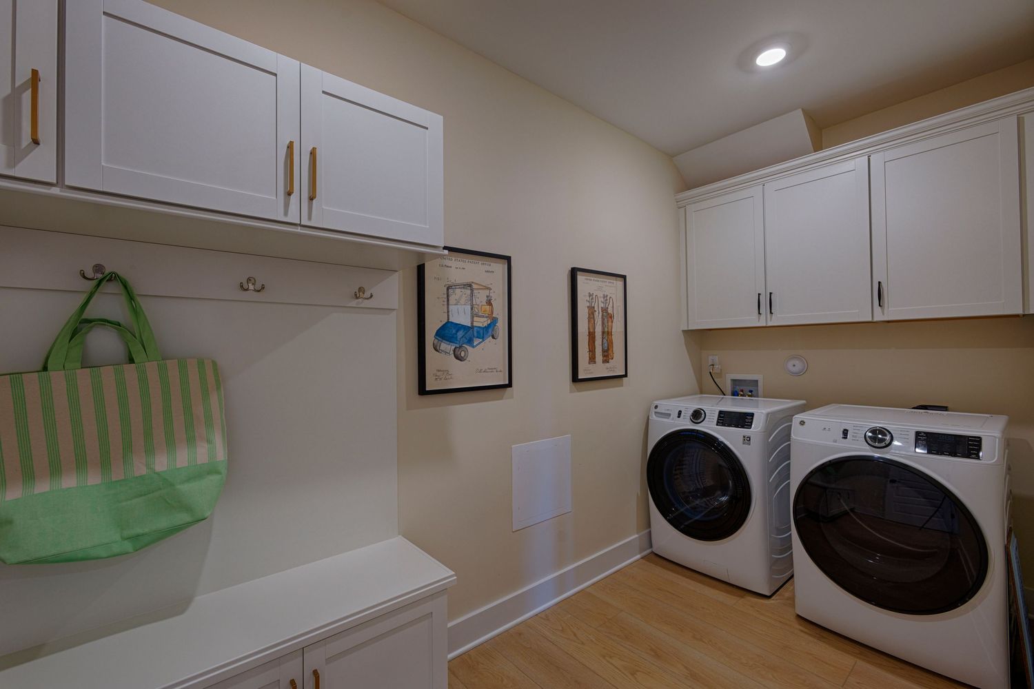 Modern laundry room with white cabinets, washer and dryer, hardwood floors, and decorative artwork on beige walls.Richmond VA