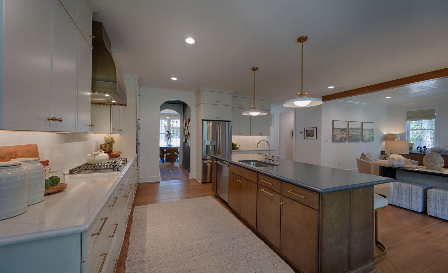 Modern kitchen with white cabinets, dark island, pendant lights, and open layout leading to living area.