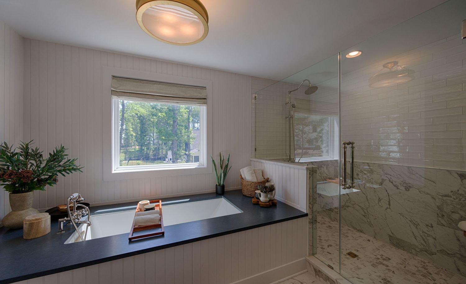 Elegant bathroom featuring a soaking tub with dark surround, glass-enclosed marble shower, and a bright window.