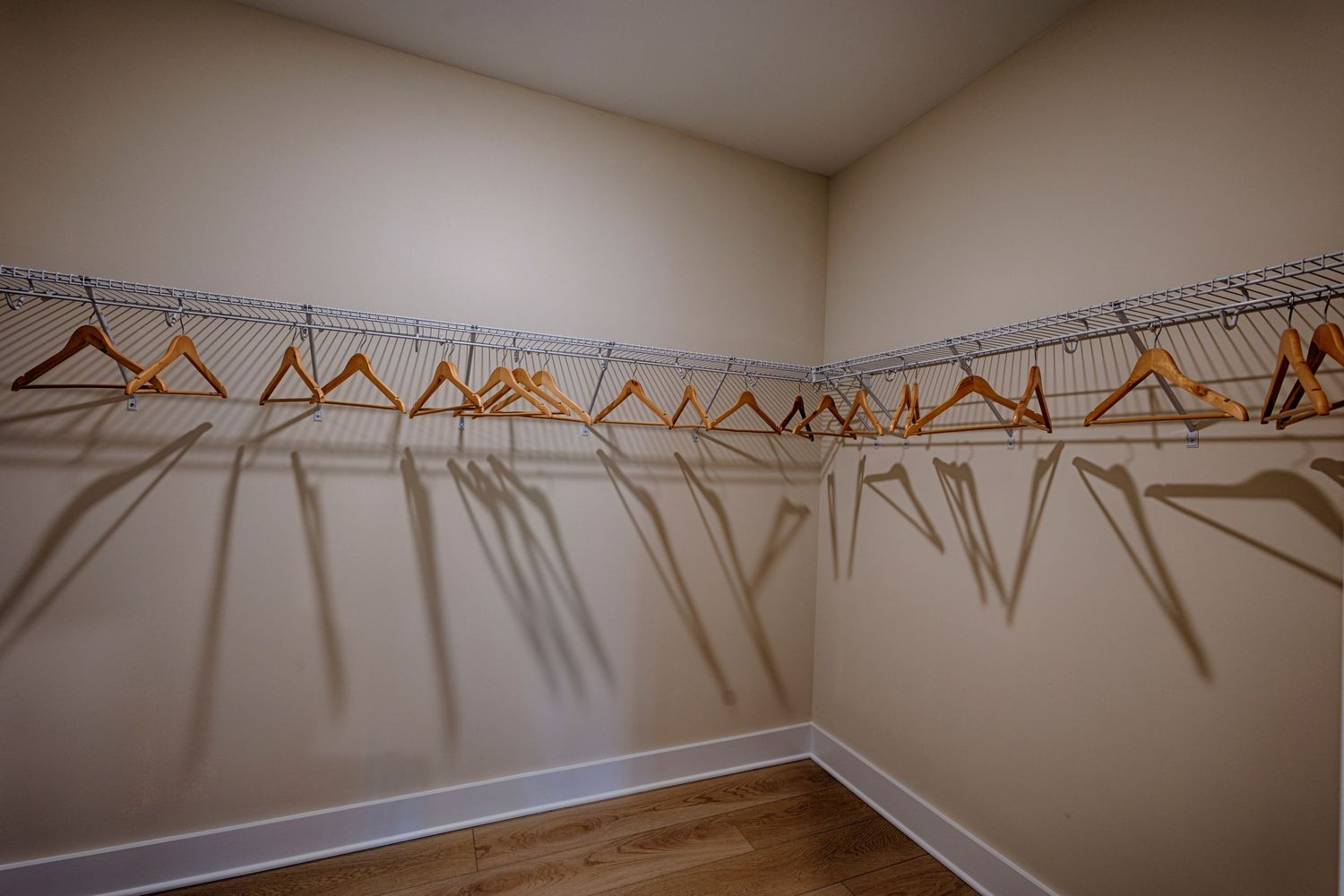 Spacious walk-in closet with wire shelving system and wooden hangers on beige walls with hardwood floors.Richmond, Virginia.