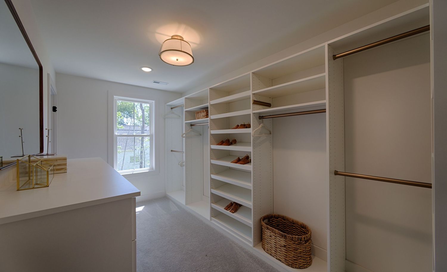 Spacious walk-in closet with white built-in shelving, hanging rods, wicker basket, and natural light from window.