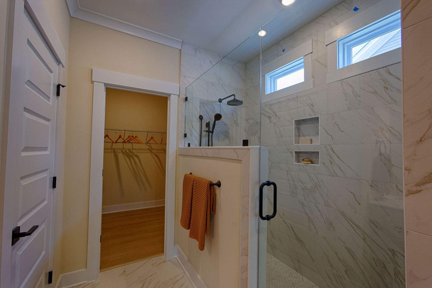 Luxury marble tile walk-in shower with glass door, built-in niche, rain showerhead, and adjacent walk-in closet.Richmond, Virginia.