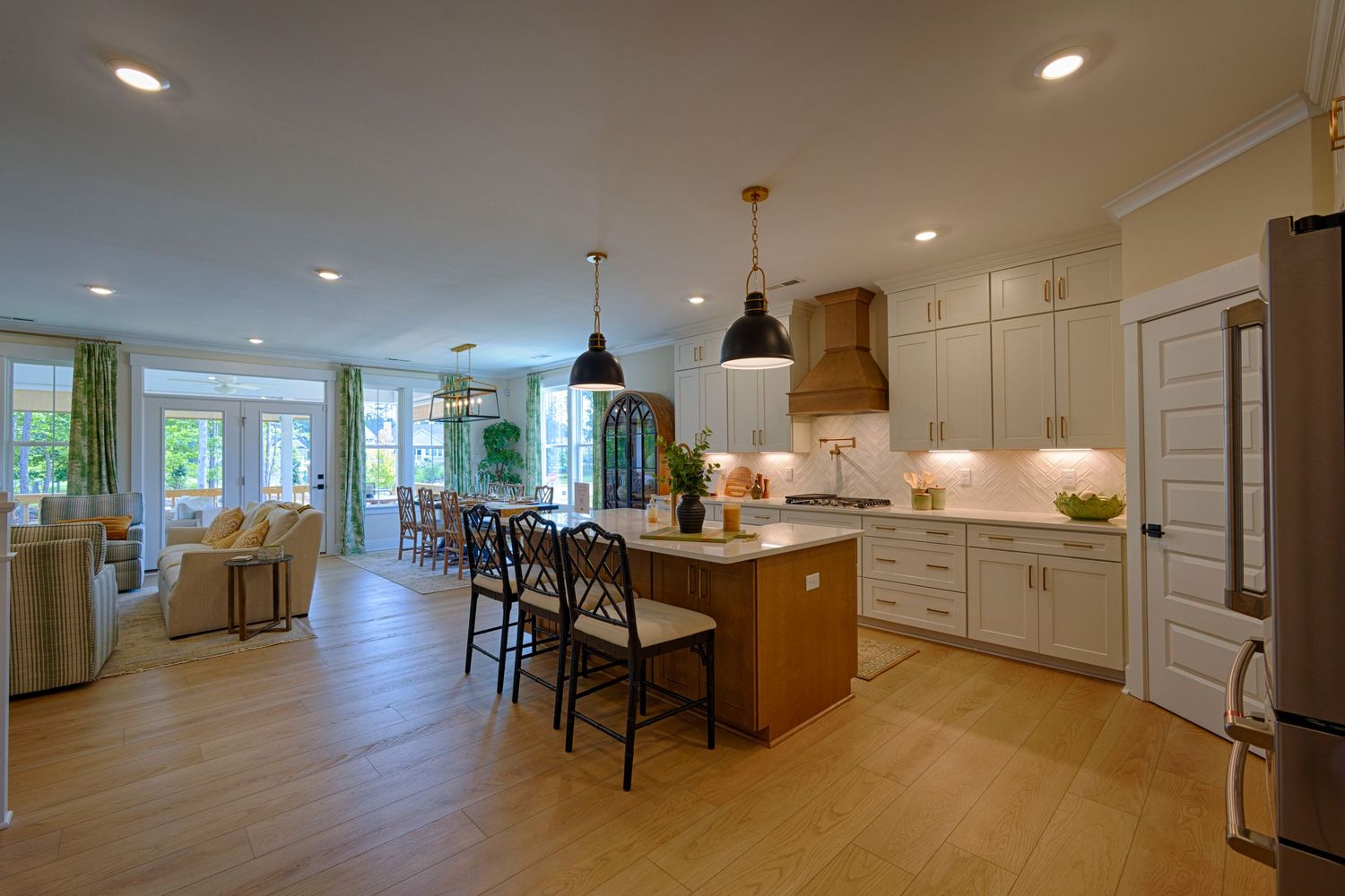 Open-concept kitchen with white cabinets, island seating, pendant lights, and hardwood floors flowing. Real Estate Photography Richmond VA