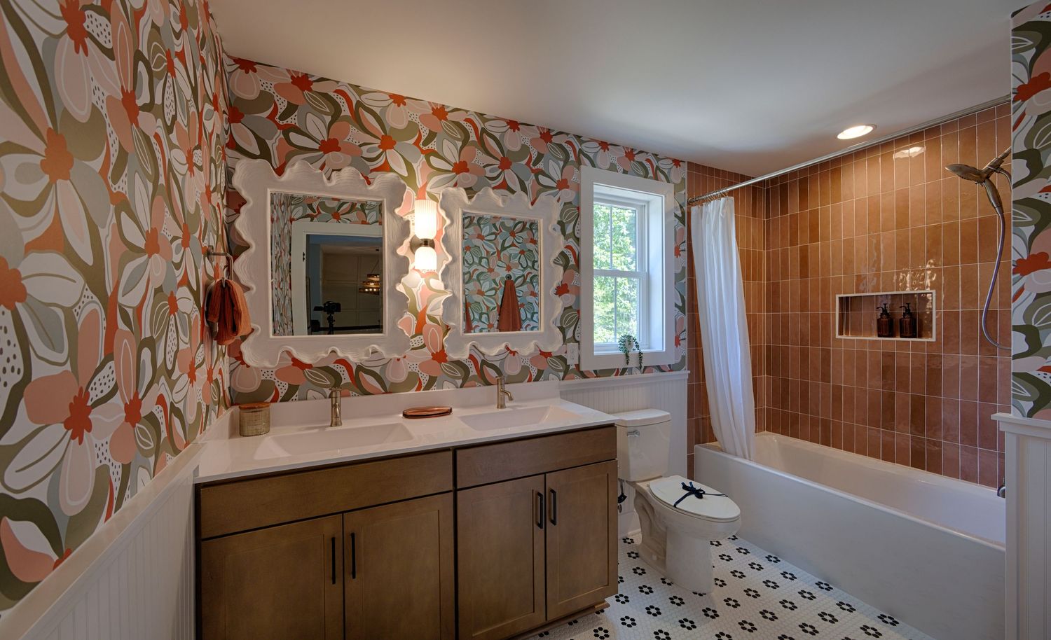 Stylish bathroom featuring bold floral wallpaper, dual vanity, tiled shower-tub combo, and patterned floor tiles.