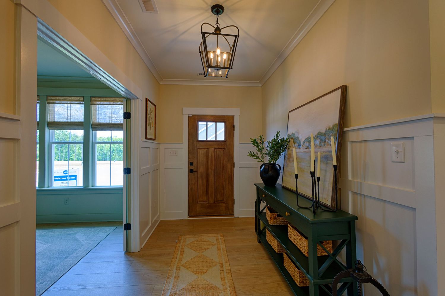Elegant home entryway with wainscoting, lantern chandelier, wood front door, and green console table with candles.Richmond VA