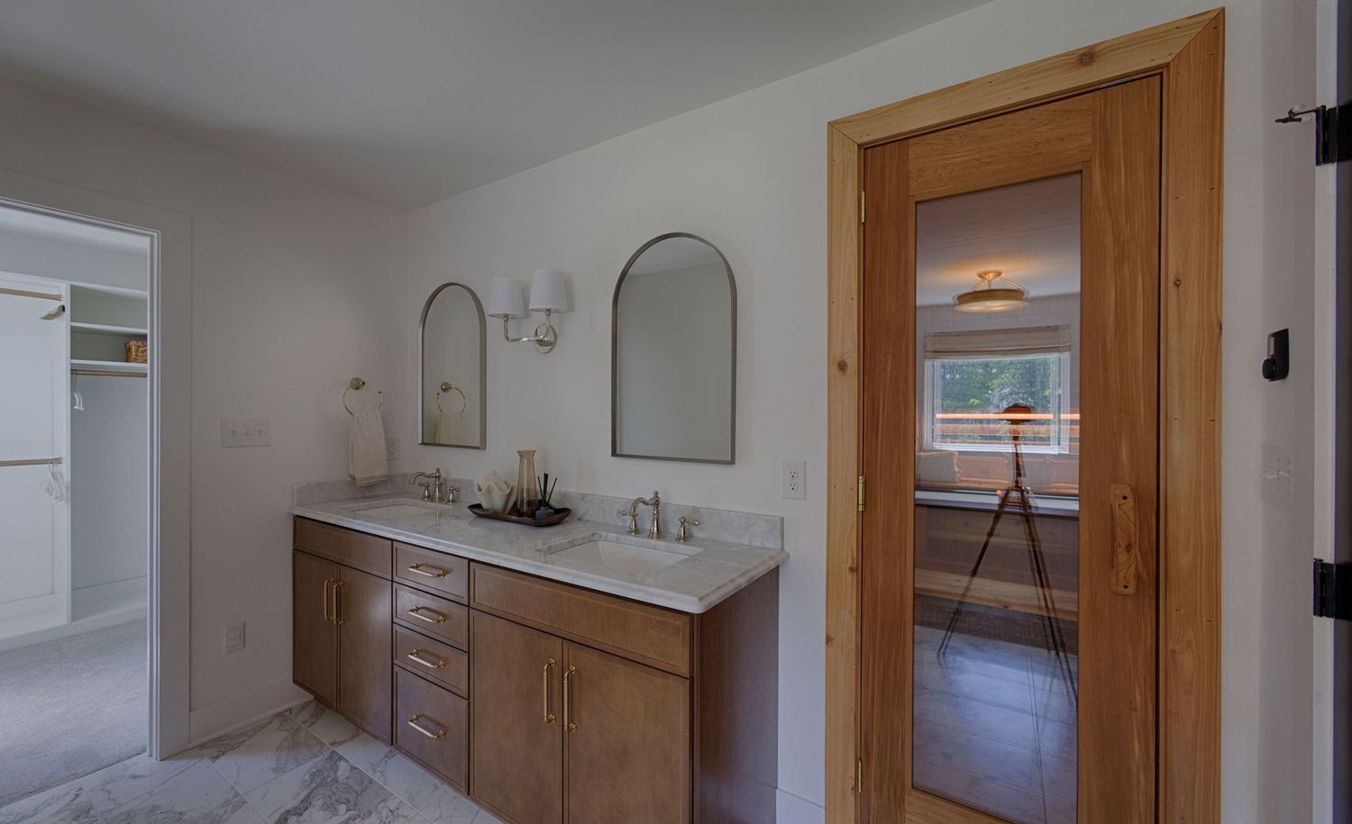 Master bathroom with dual-sink wood vanity, arched mirrors, and a barn door leading to an adjacent bedroom.