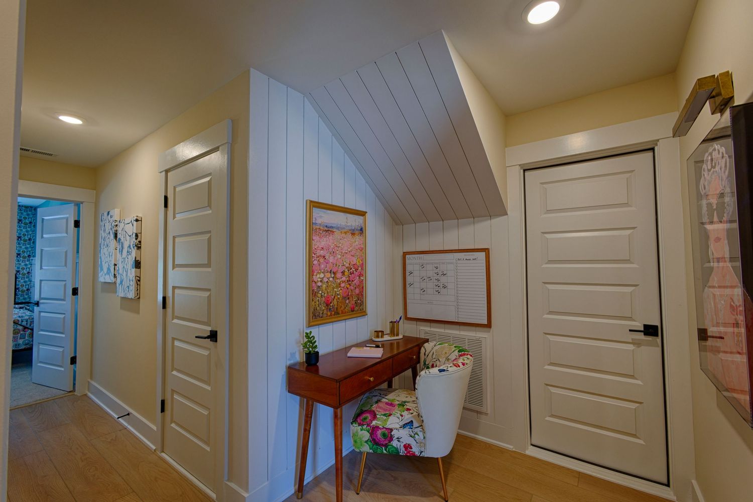 Cozy hallway nook with sloped ceiling, small desk, floral chair, and white shiplap accent wall.Richmond, Virginia.