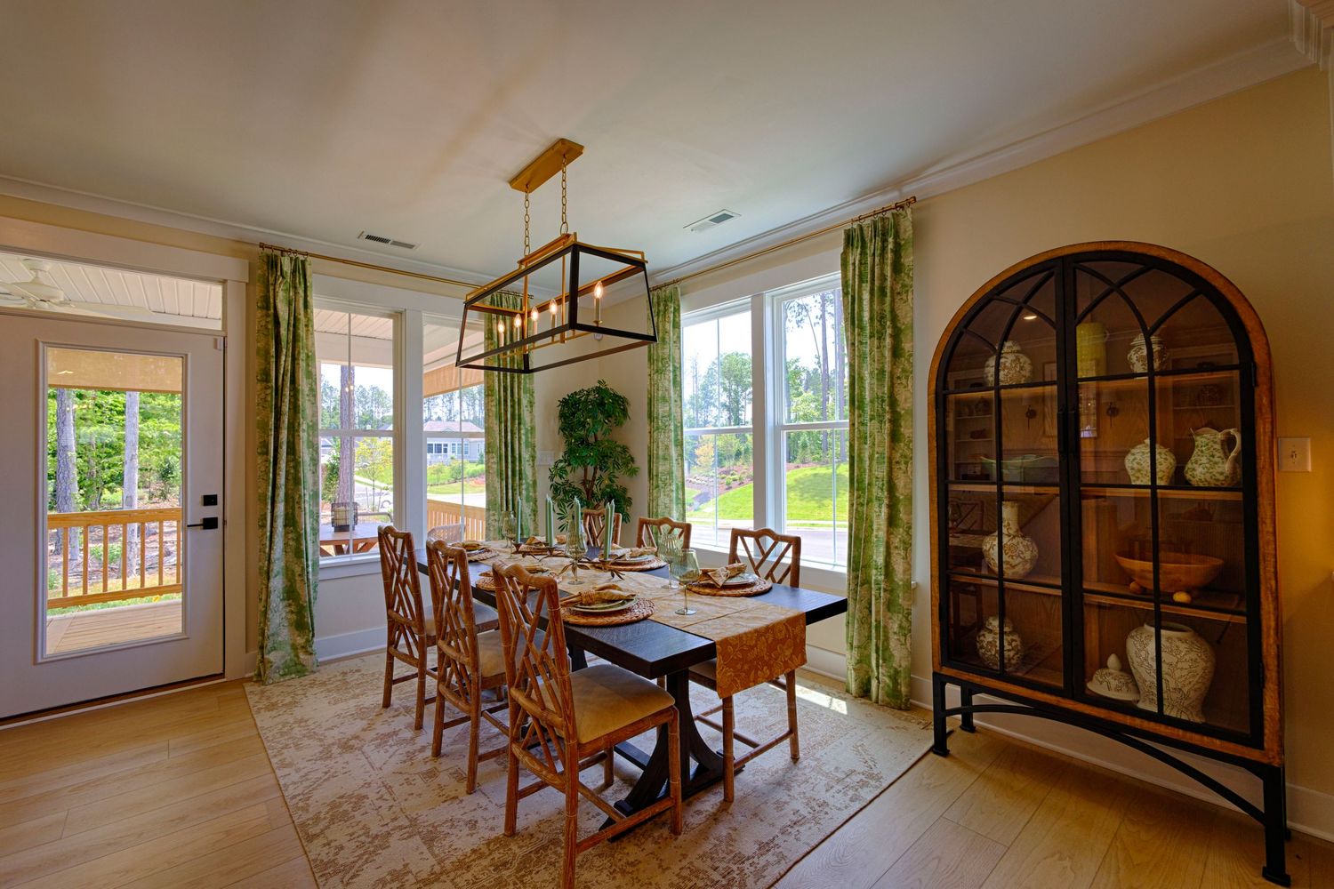 Elegant dining room with wooden table, arched china cabinet, green curtains, and natural light from large windows.Richmond, Virginia.