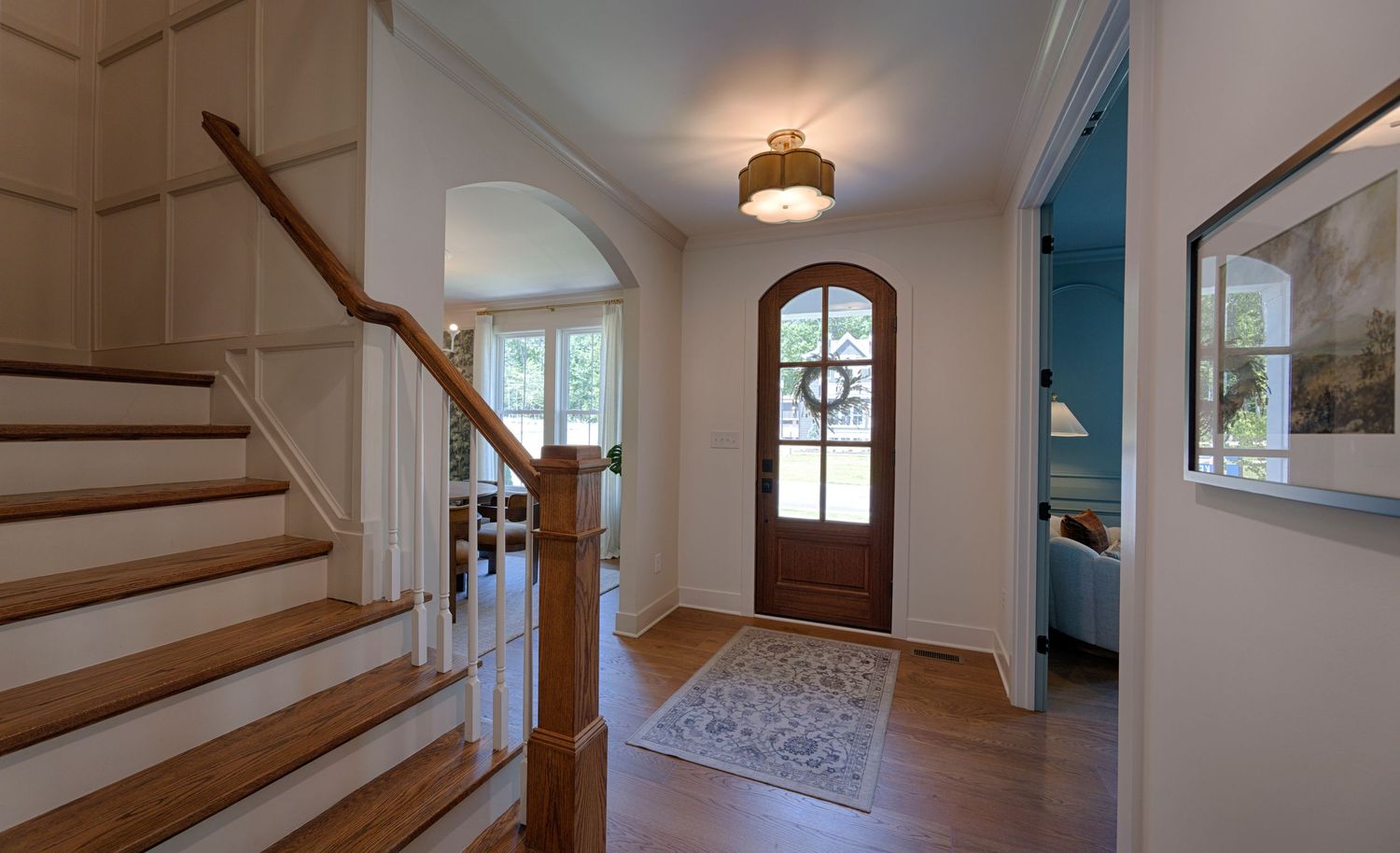 Bright foyer with hardwood floors, arched front door, staircase, and elegant ceiling light fixture.