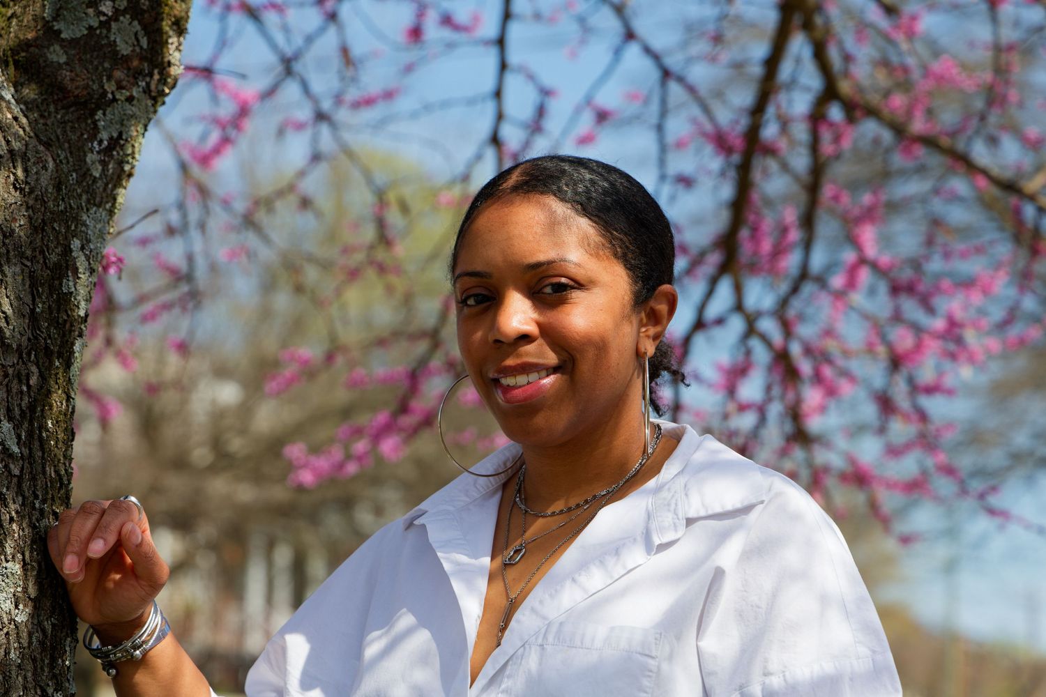 A person in white shirt smiles near blooming pink cherry blossom trees. downtown Richmond, Virginia, RVA