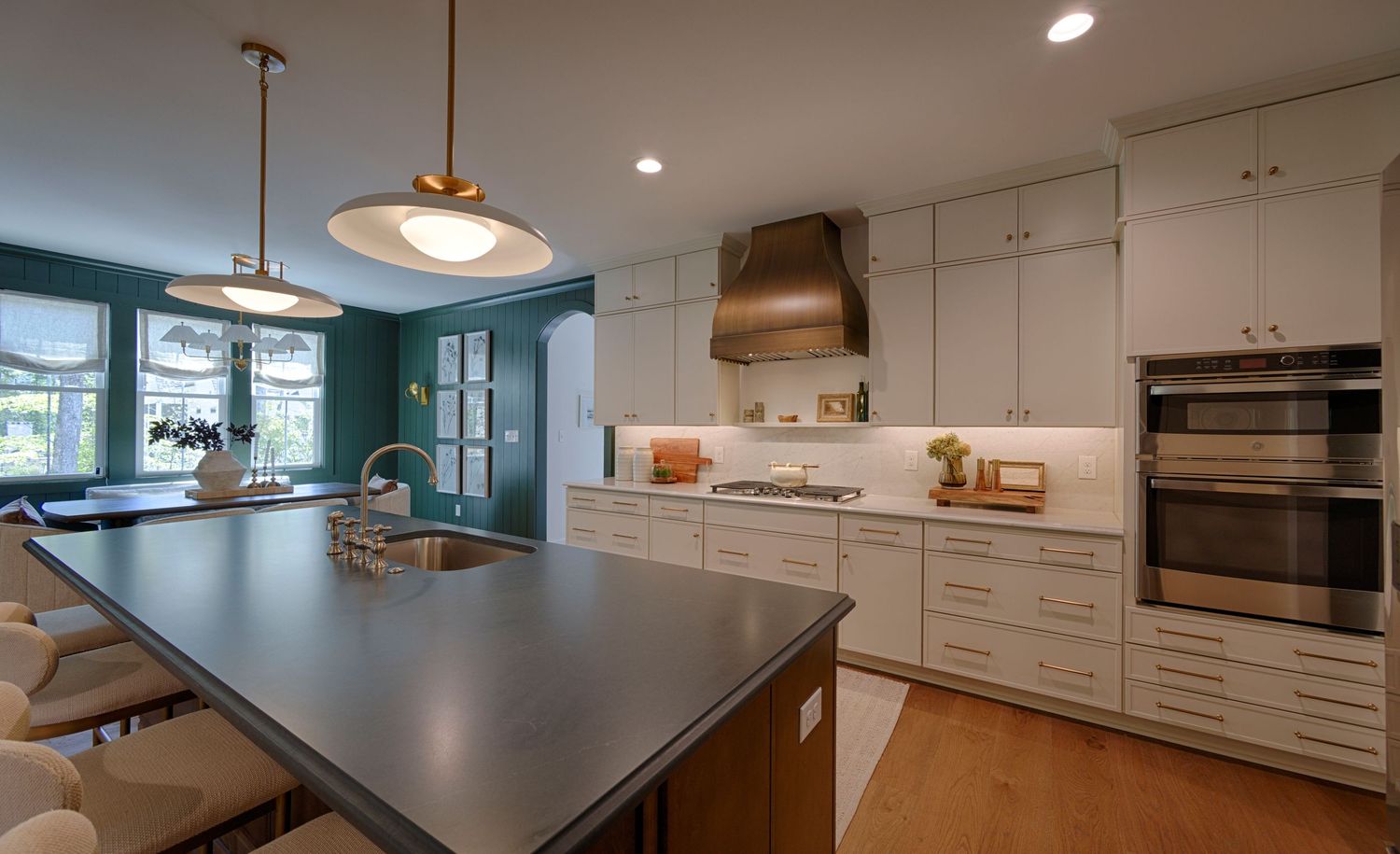 Modern kitchen with white cabinets, gray island, pendant lights, stainless appliances, and teal accent wall.