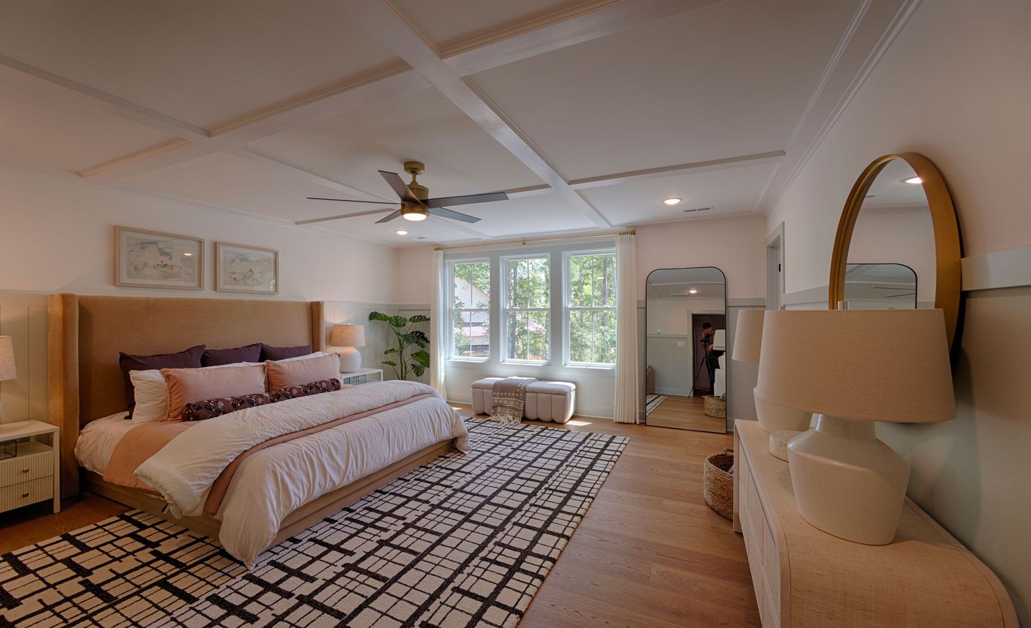 Spacious master bedroom with coffered ceiling, ceiling fan, hardwood floors, patterned area rug, and large windows.