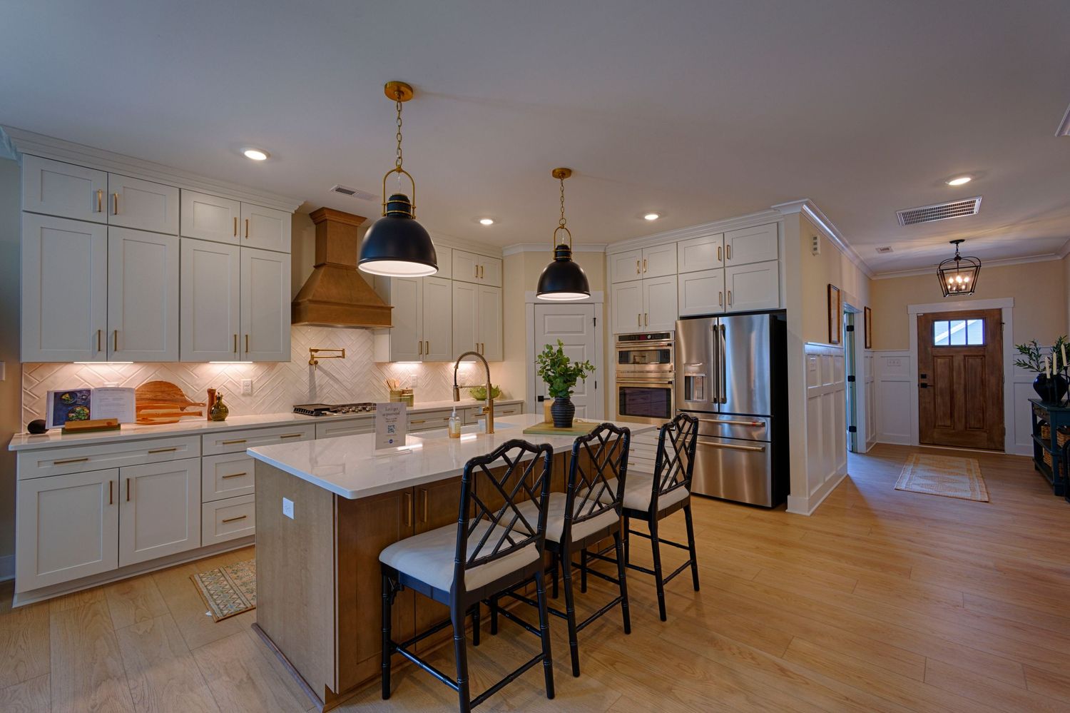 Modern white kitchen with island seating, pendant lights, stainless appliances, and hardwood floors. Real Estate Photography