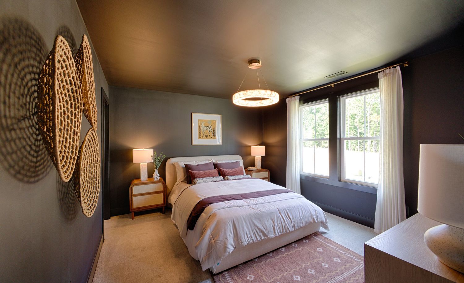 Elegant bedroom with dark walls, circular woven wall art, pendant light, and neutral bedding with burgundy accents.