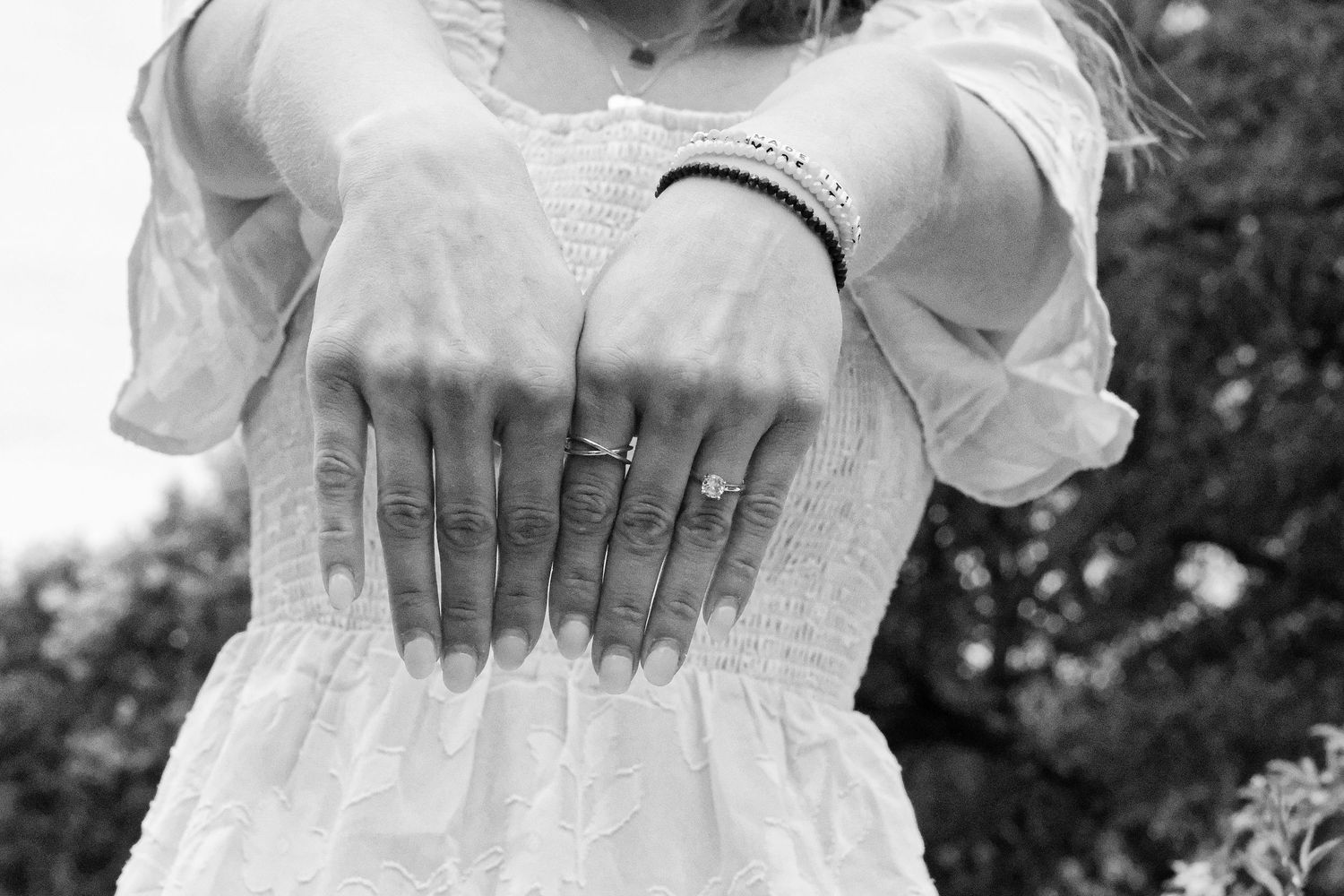 Woman in white dress displaying rings on fingers and a bracelet on wrist, black and white photo.