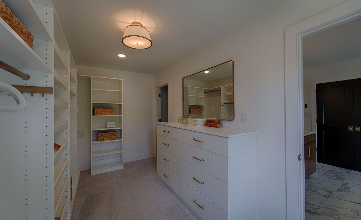 Spacious walk-in closet with white built-in shelving, gold hardware dresser, and soft carpet flooring.