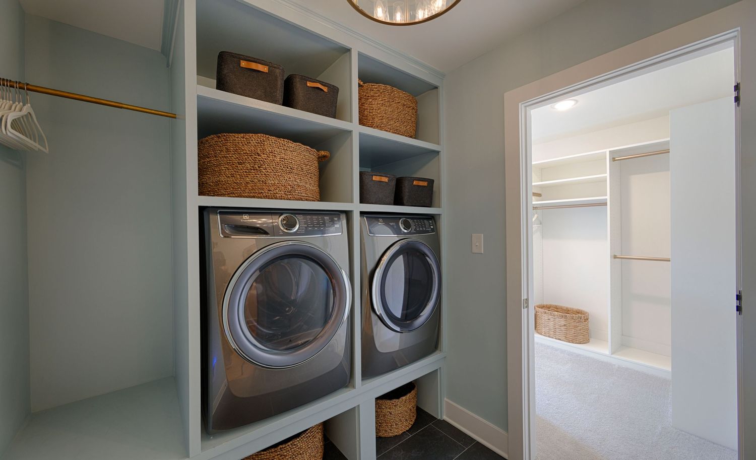 Modern laundry room with front-load washer and dryer, built-in shelving, wicker baskets, and access to a walk-in closet.
