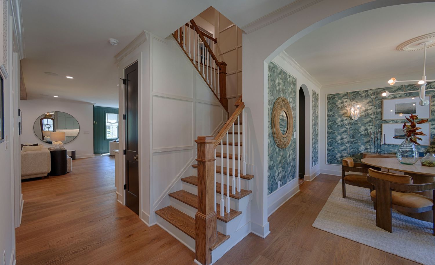 Elegant home entryway with wood staircase, hardwood floors, arched doorway, and decorative wallpaper accent wall.