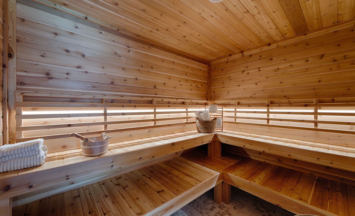 Spacious wooden sauna interior with tiered benches, bucket, and ladle, featuring natural pine wood walls and ceiling.