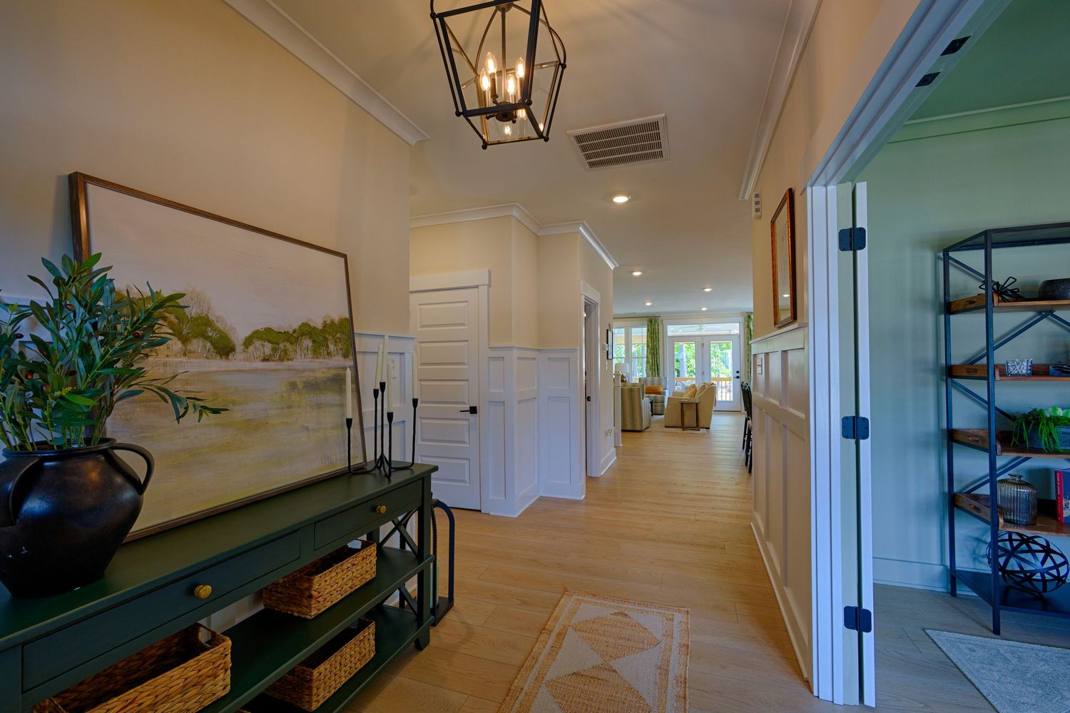 Elegant hallway with wainscoting, lantern chandelier, green console table, and hardwood floors leading to bright living area.Richmond VA