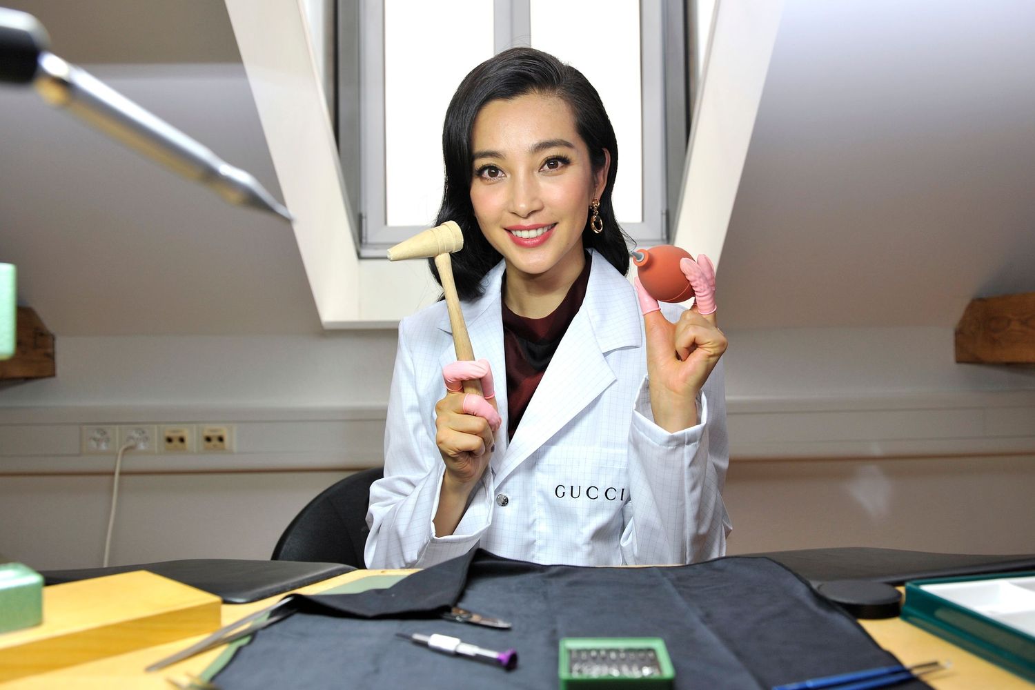 Fan Bingbing in Gucci lab coat holding crafting tools at a workshop desk.