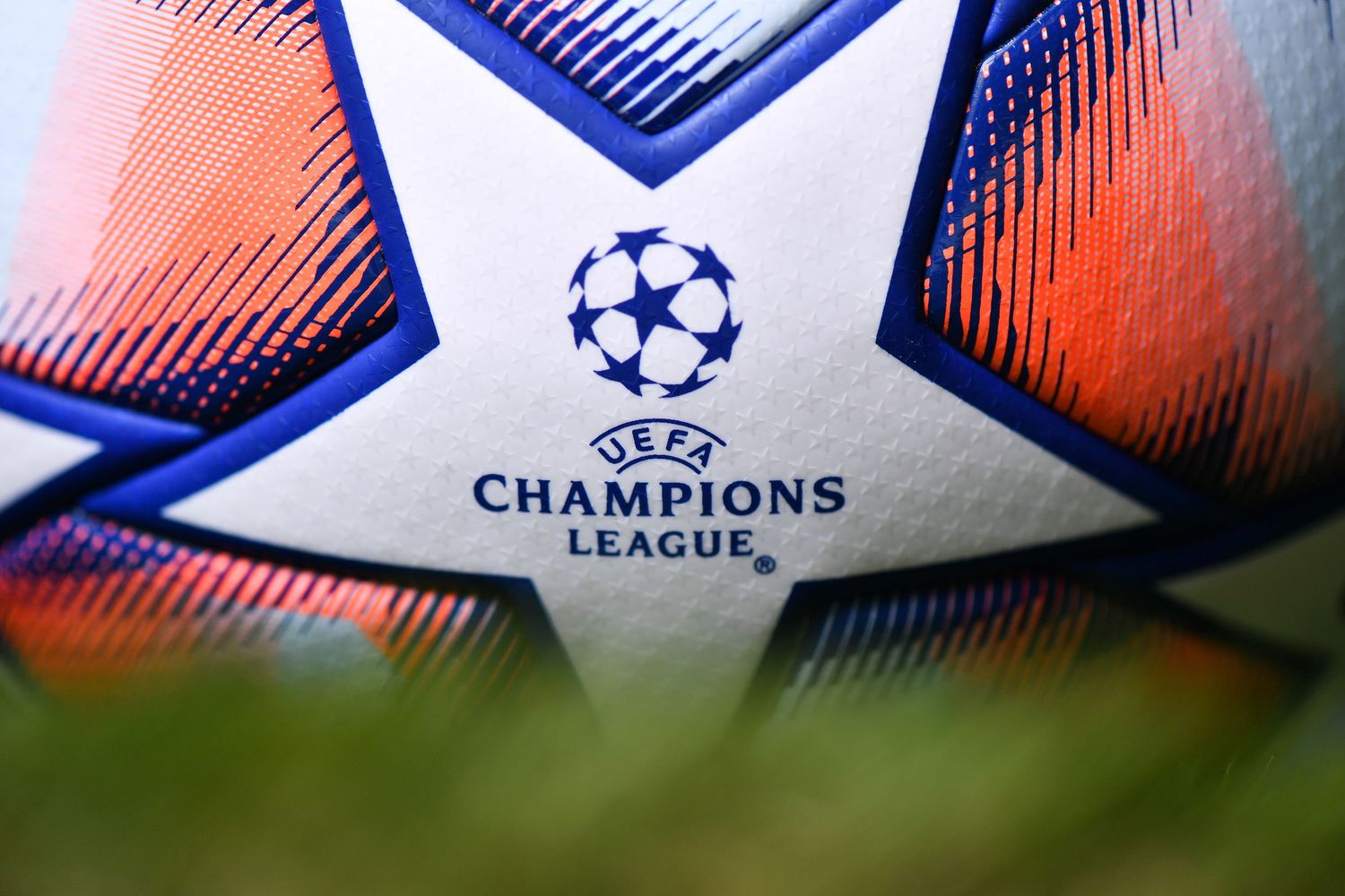 Official UEFA Champions League soccer ball with colorful design resting on green grass.