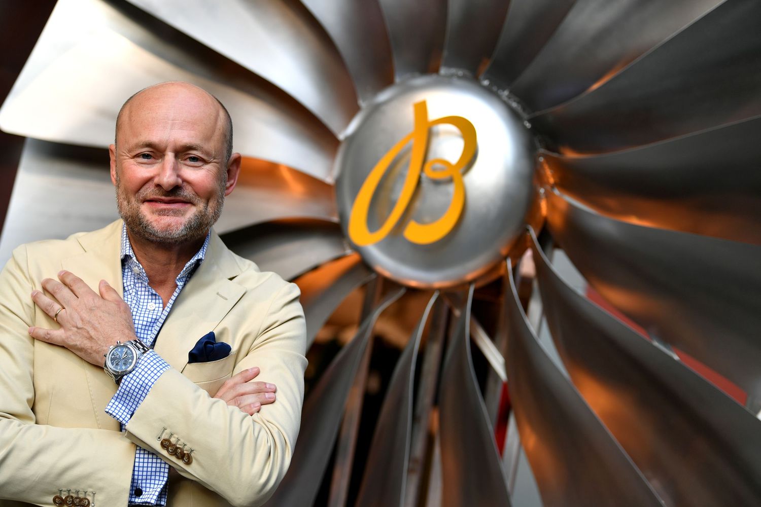 Georges Kern in beige blazer posing in front of a large jet engine turbine.