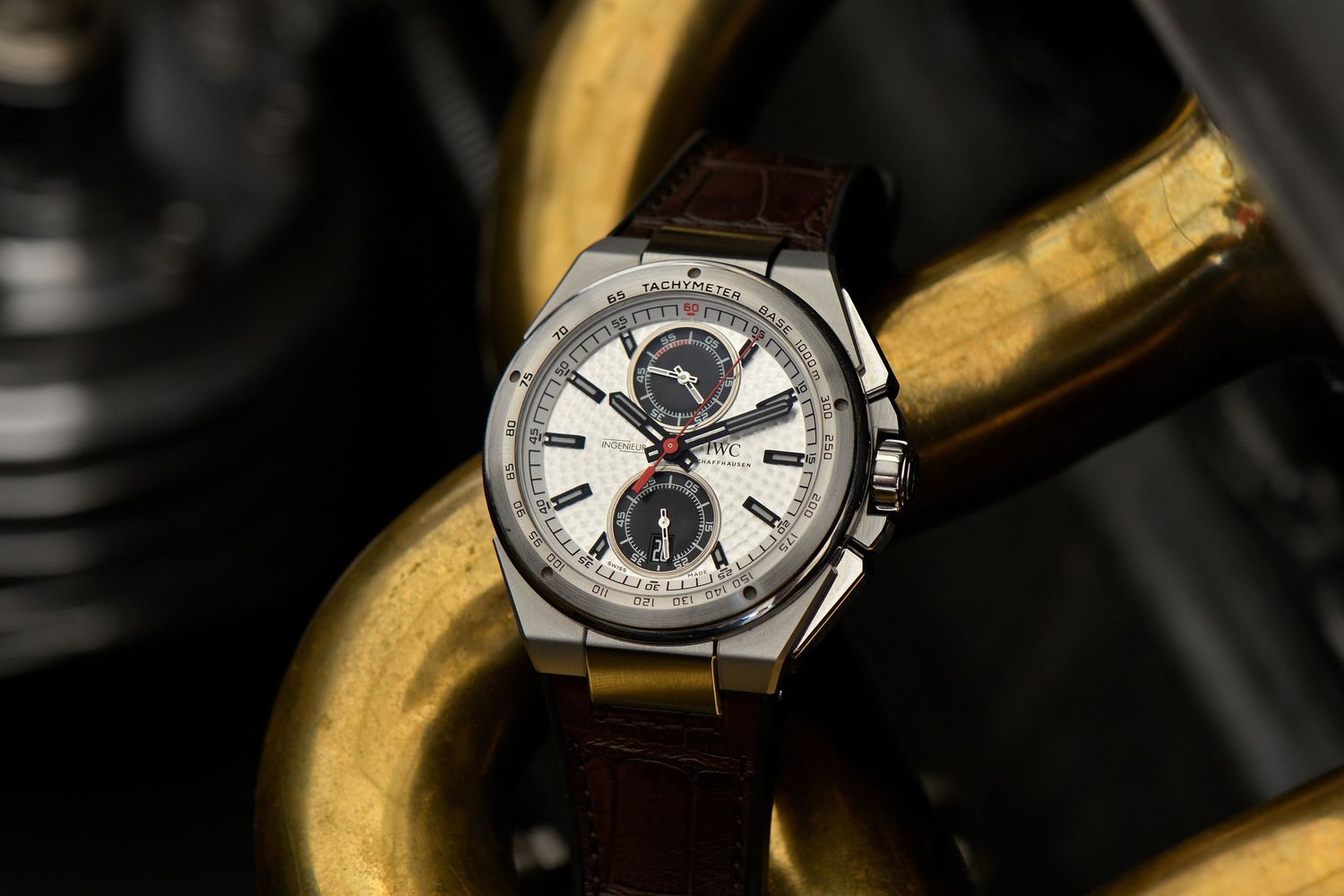 IWC watch with white dial and brown leather strap on golden metallic engine surface.