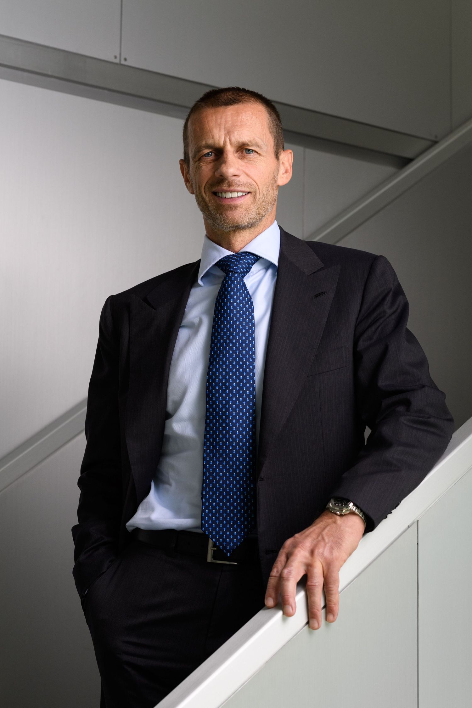 Aleksander Ceferin leans on a staircase railing smiling.