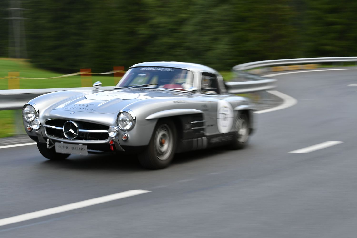 Classic silver Mercedes-Benz 300SL coupe racing on wet asphalt road at speed.