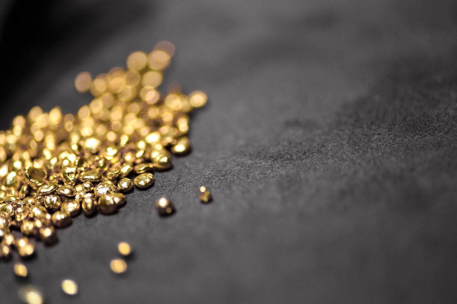 Scattered shiny gold granules on dark textured surface close-up macro shot.