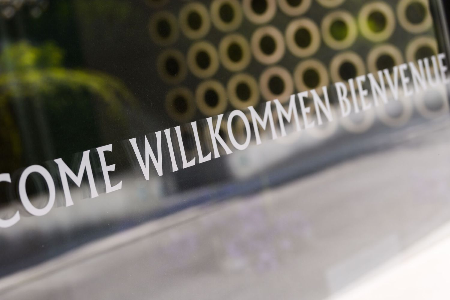 Welcome sign in multiple languages including English, German and French on a glass surface.