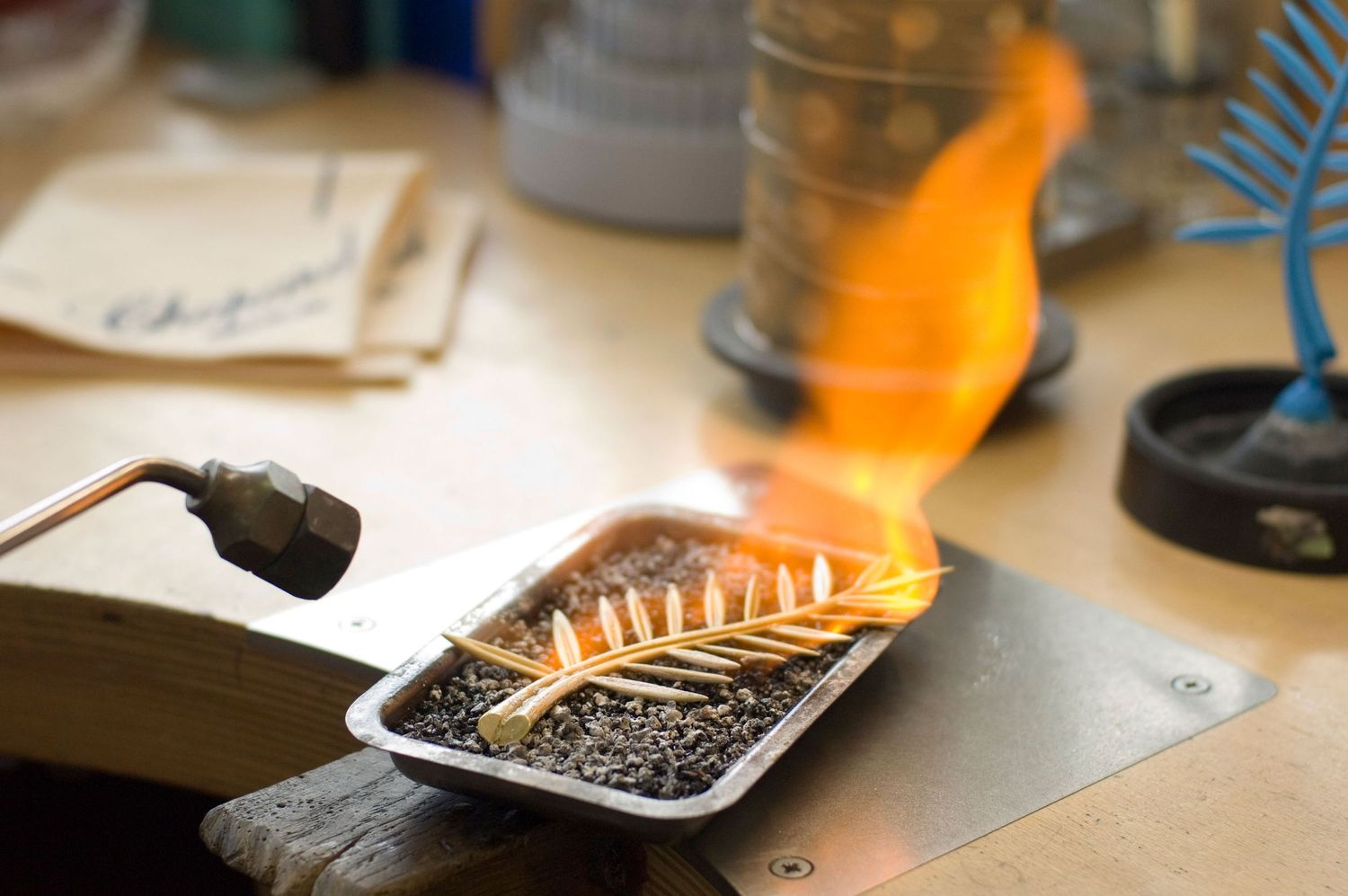 Chopard Cannes Film Festival Palme d'Or againt a metal tray with burning materials and bright orange flames in a workshop setting.