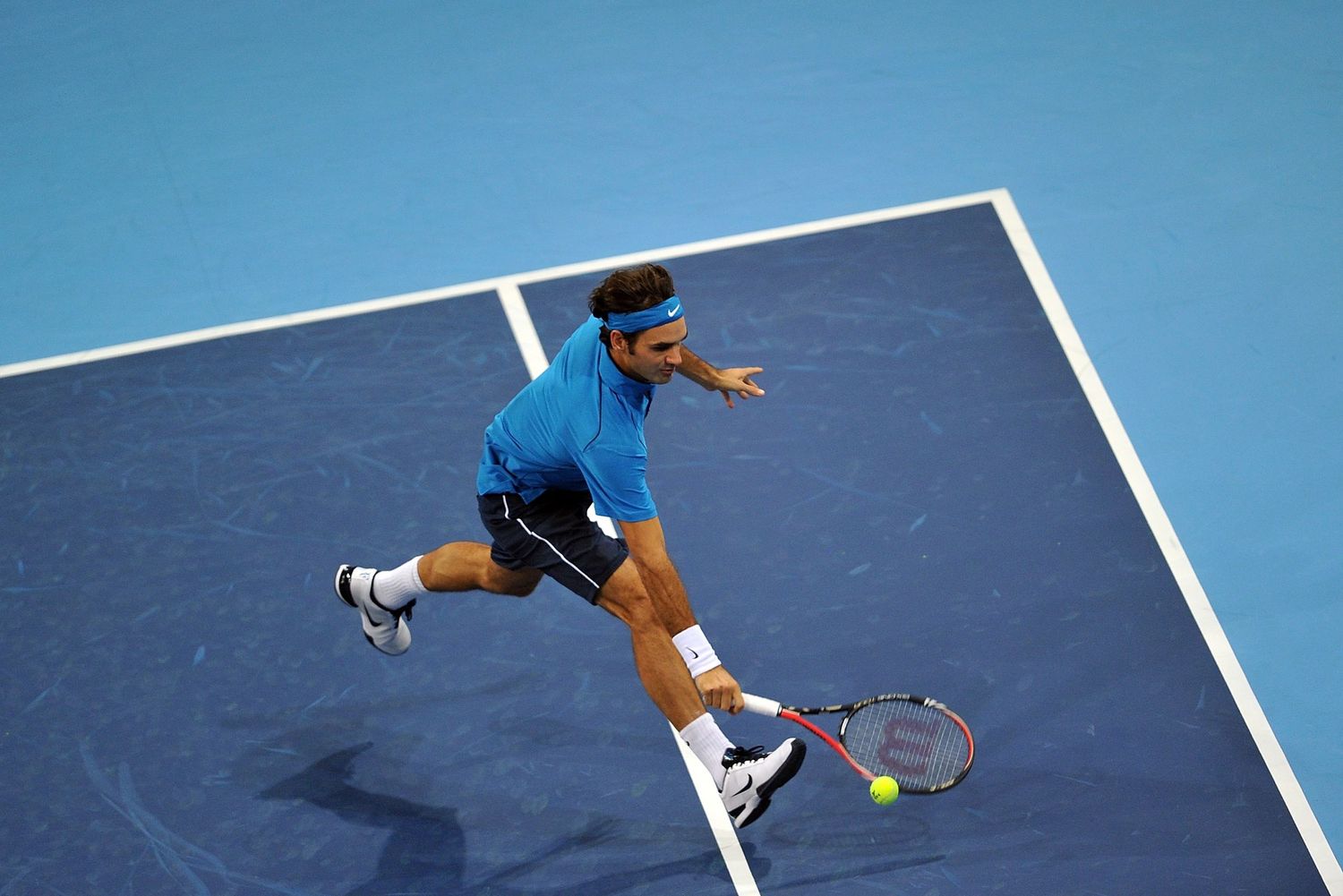 Tennis player in blue shirt lunging forward to hit a forehand shot on a blue hard court during a match.