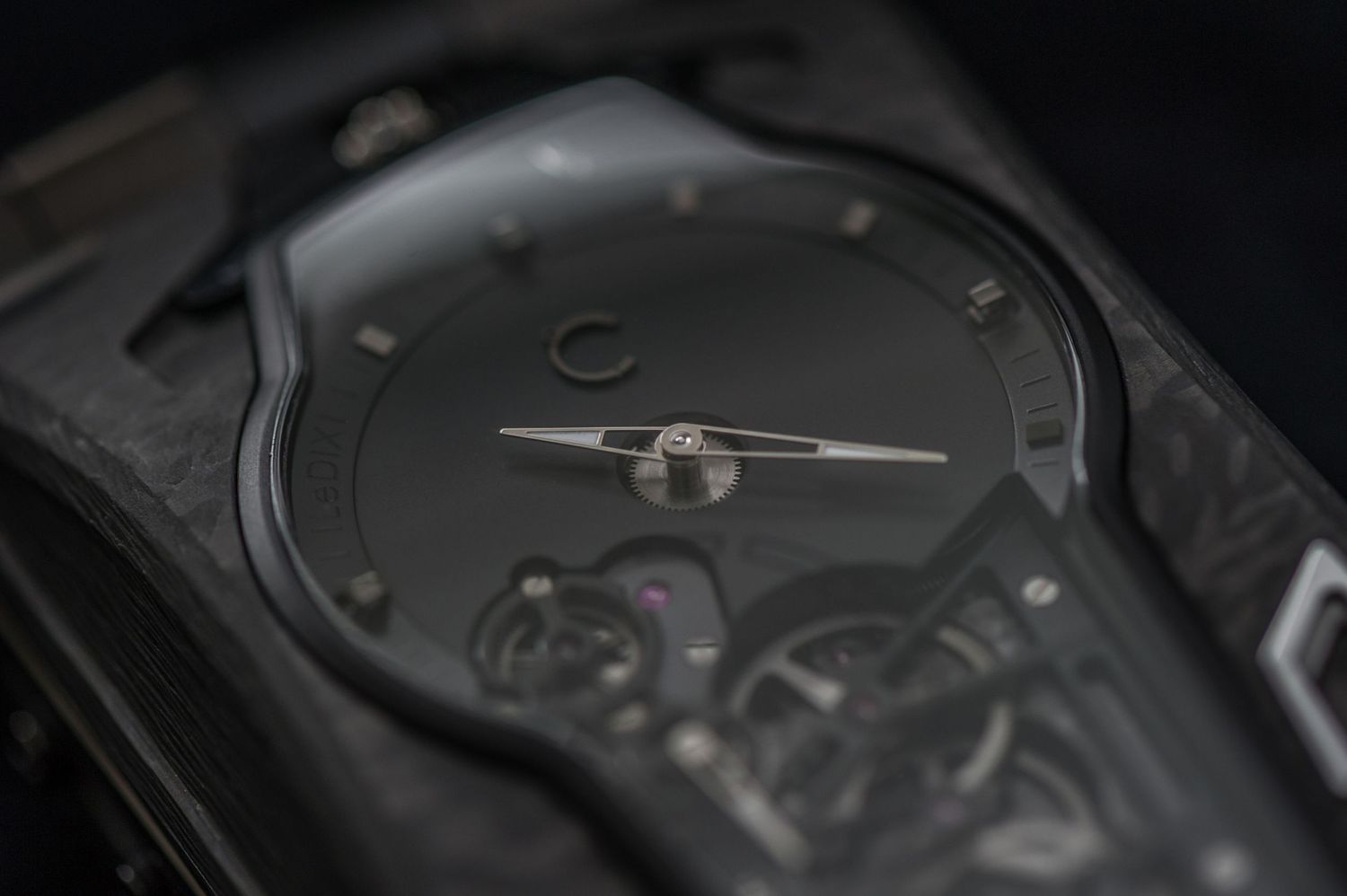 Minimalist luxury black wristwatch with skeleton movement visible through dark carbon fiber case.