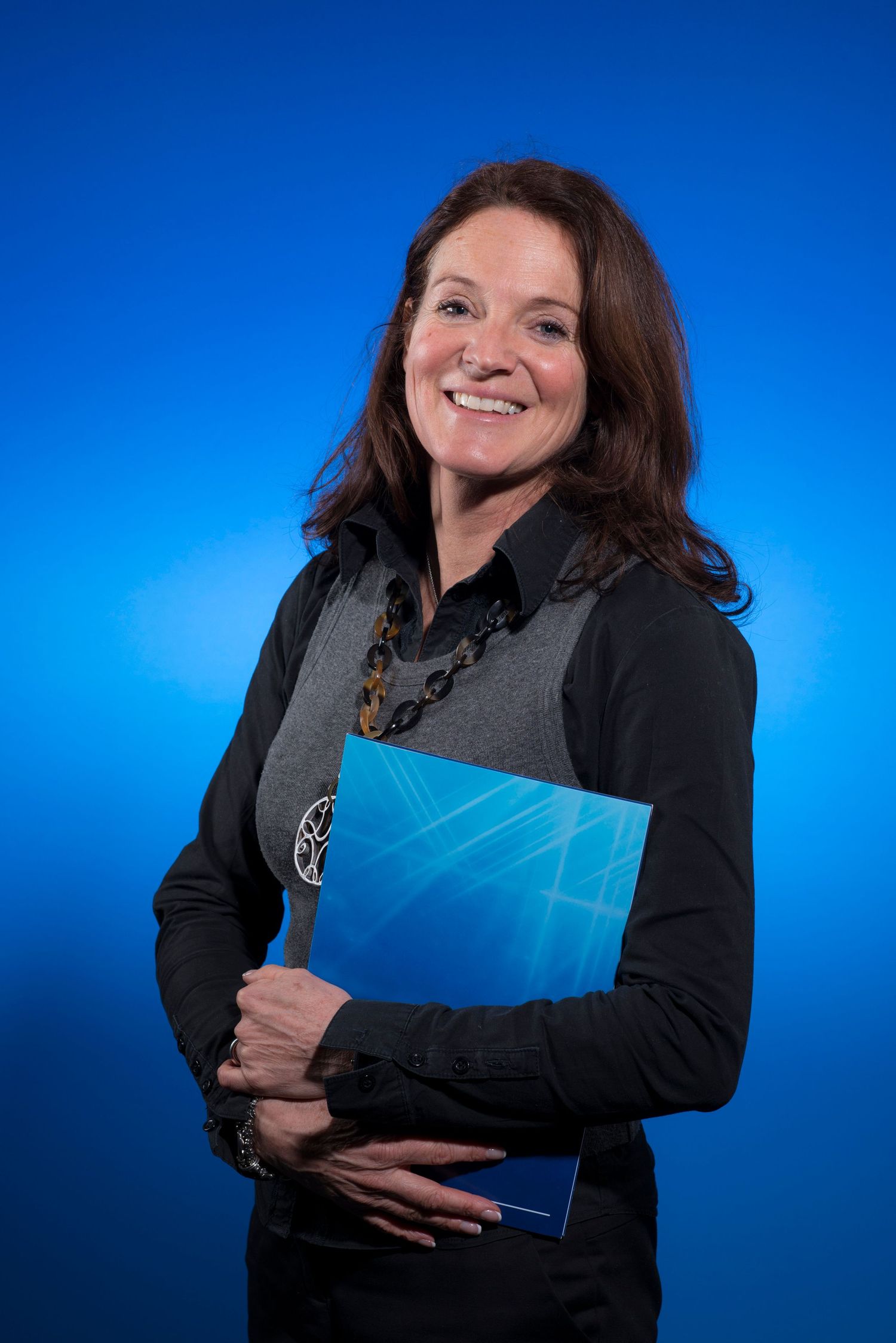 A smiling woman with brown hair holds a blue folder against a bright blue background.