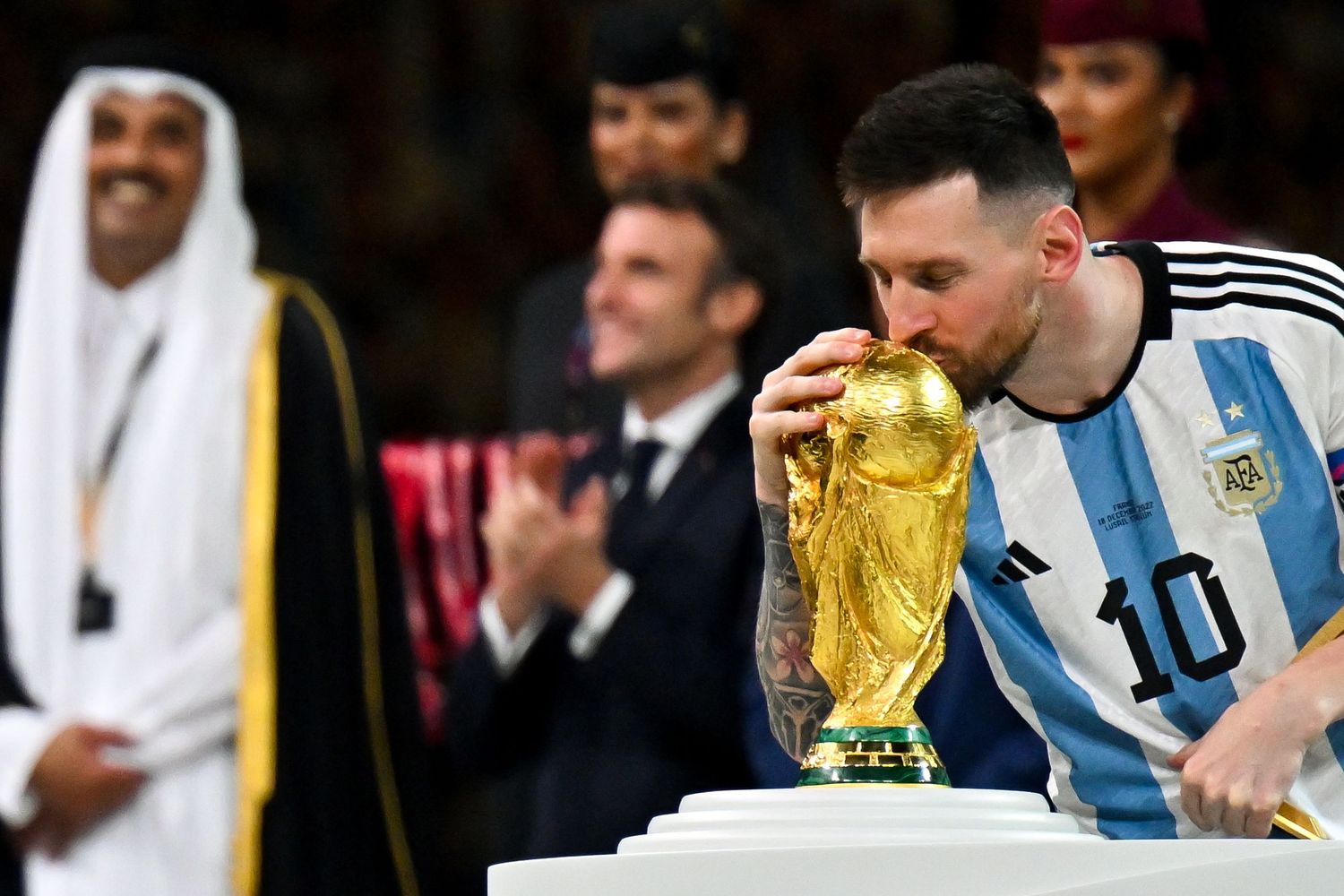 Lionel Messi in Argentina jersey kisses FIFA World Cup trophy at award ceremony.