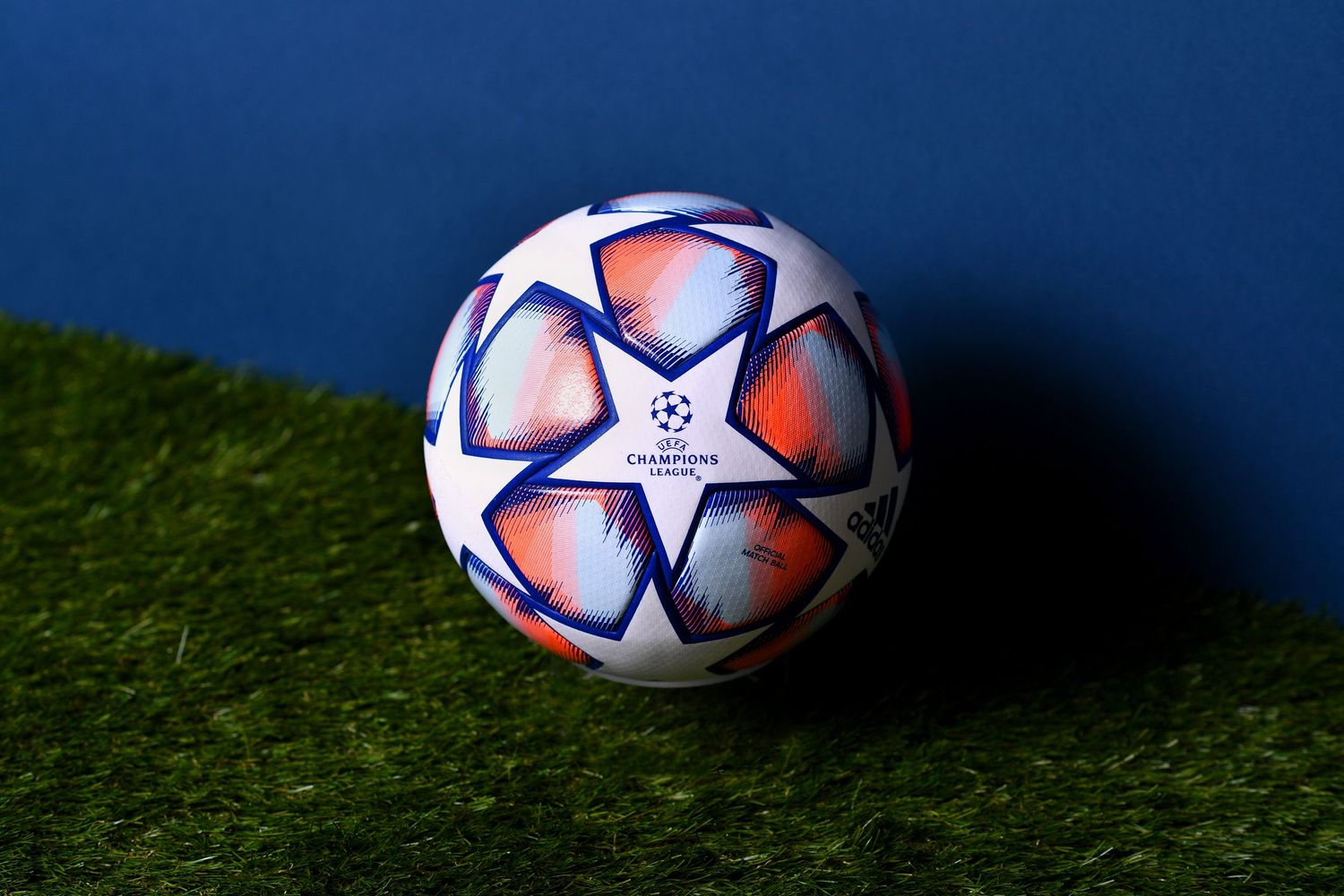 Adidas UEFA Champions League official white soccer ball on green grass with blue background.