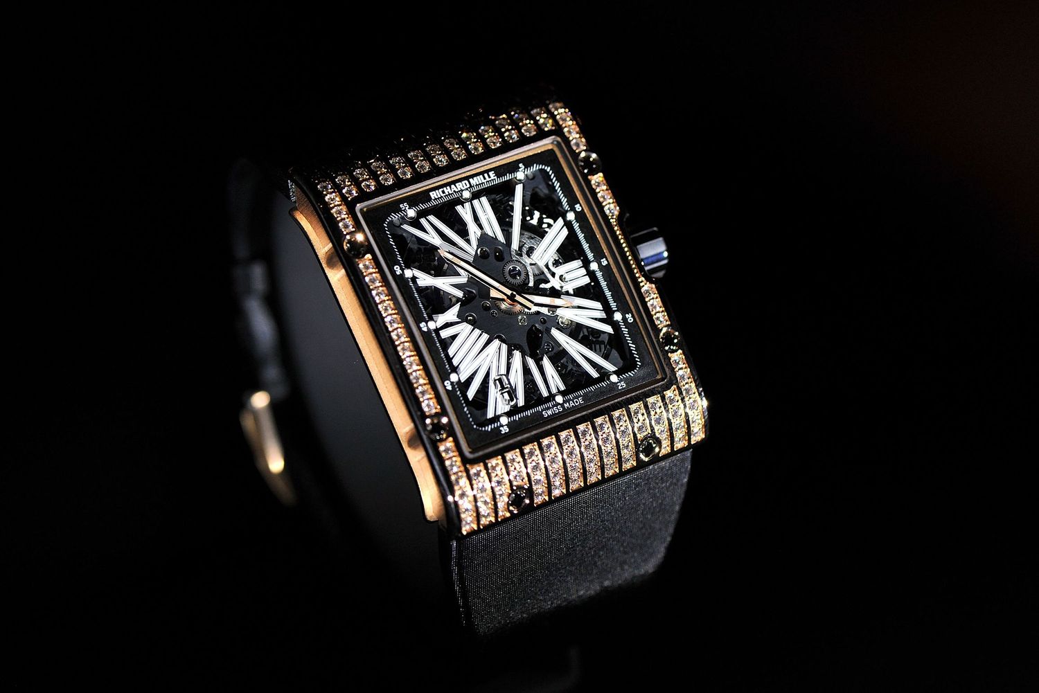 Luxury square rose gold diamond-encrusted watch with black dial on dark background.