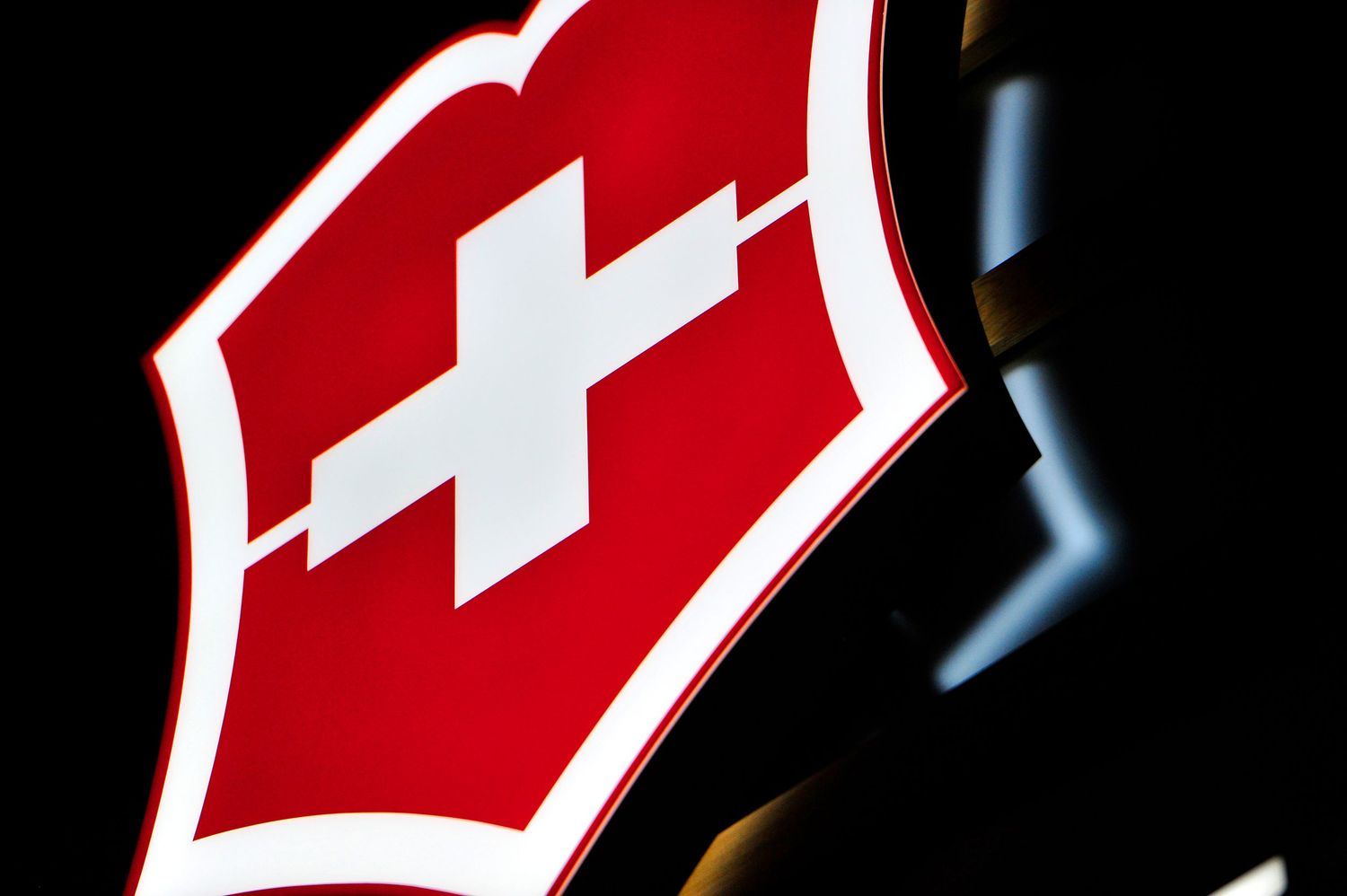 Illuminated Victorinox Swiss Army knife logo glowing red and white against a dark background.