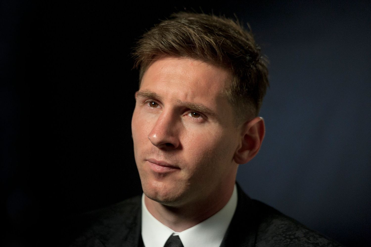 Lionel Messi wearing a dark jacket looks thoughtfully to the side.