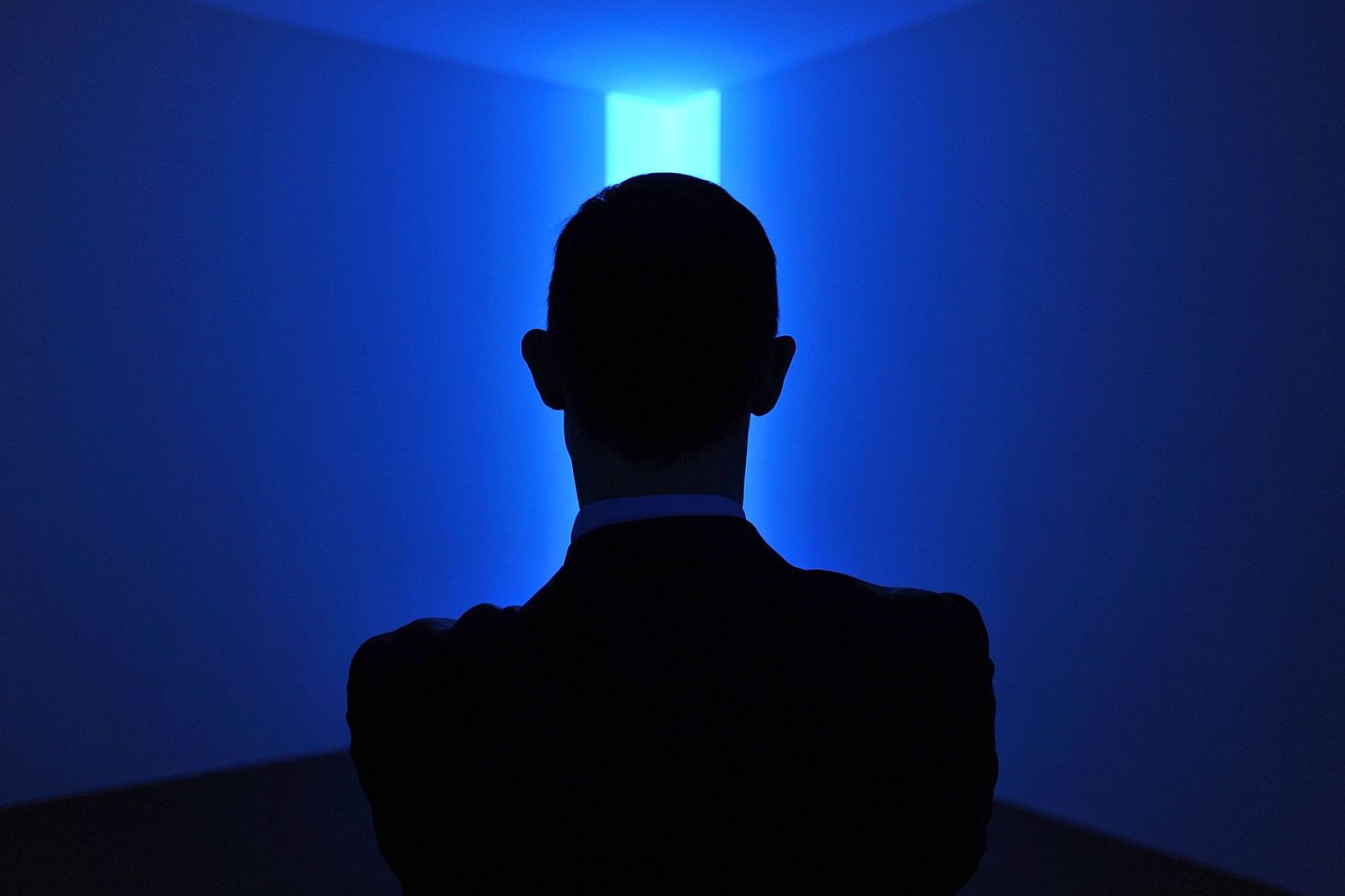 Silhouette of a person facing a glowing blue light installation in a dark room.