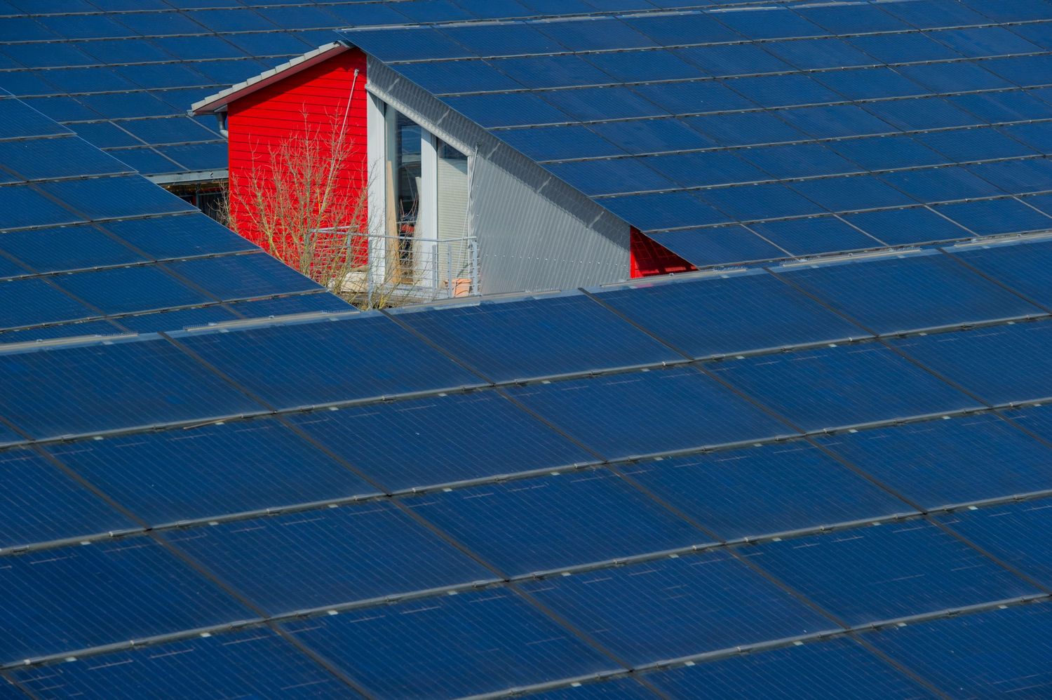 Red dormer window surrounded by large blue solar panel array on rooftop.
